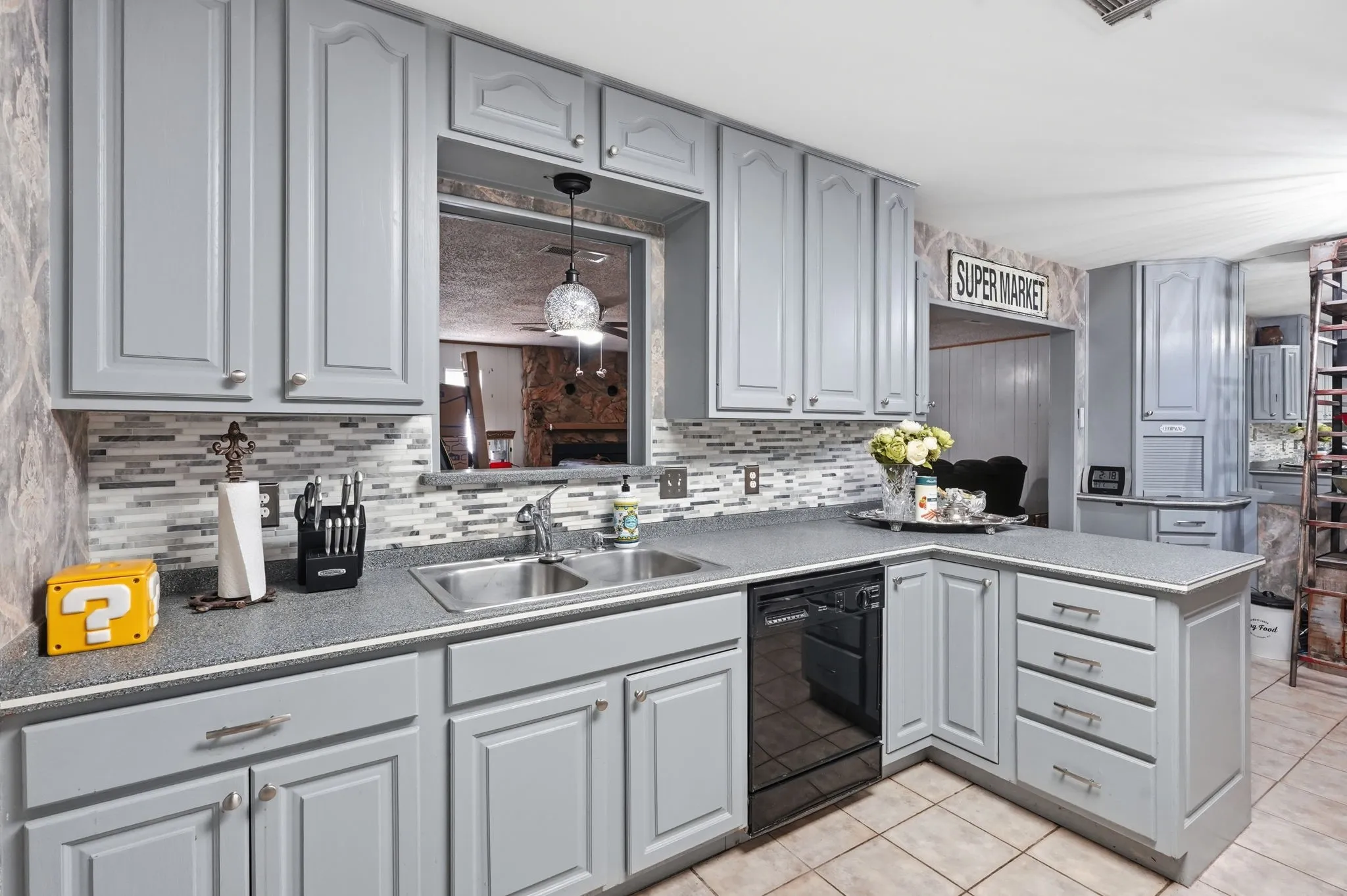 Light gray cabinetry with brushed nickel hardware, L-shaped countertop, dual basin stainless steel sink, black dishwasher, and a mosaic tile backsplash