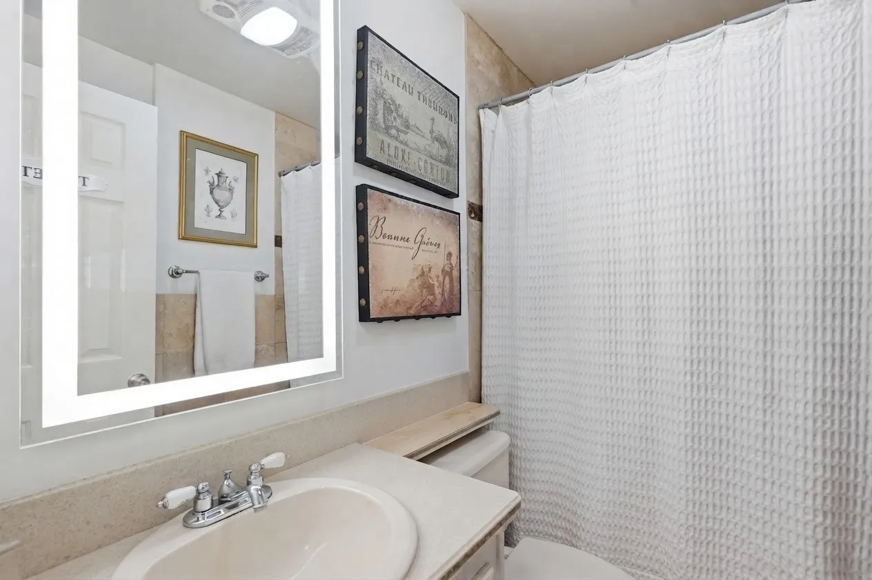 Backlit vanity mirror, single basin sink, chrome faucet, and tiled shower surround