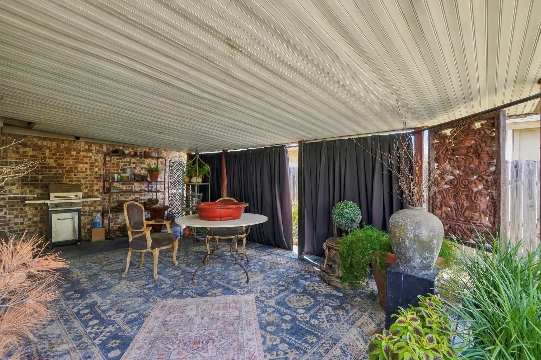 Covered patio with a corrugated ceiling, exposed brick wall, and privacy drapery