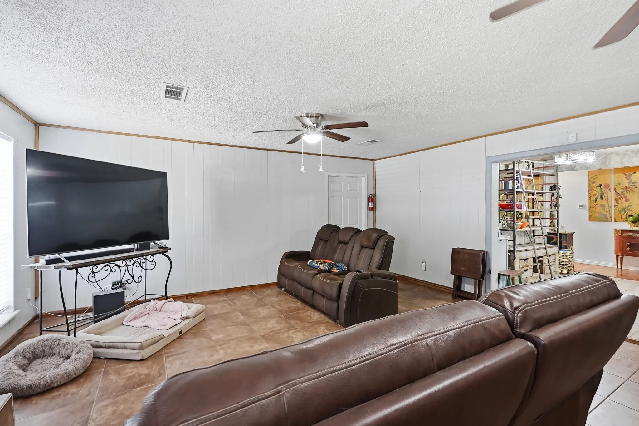 Tile flooring, white paneled walls, ceiling fan with light fixture, and an arched doorway