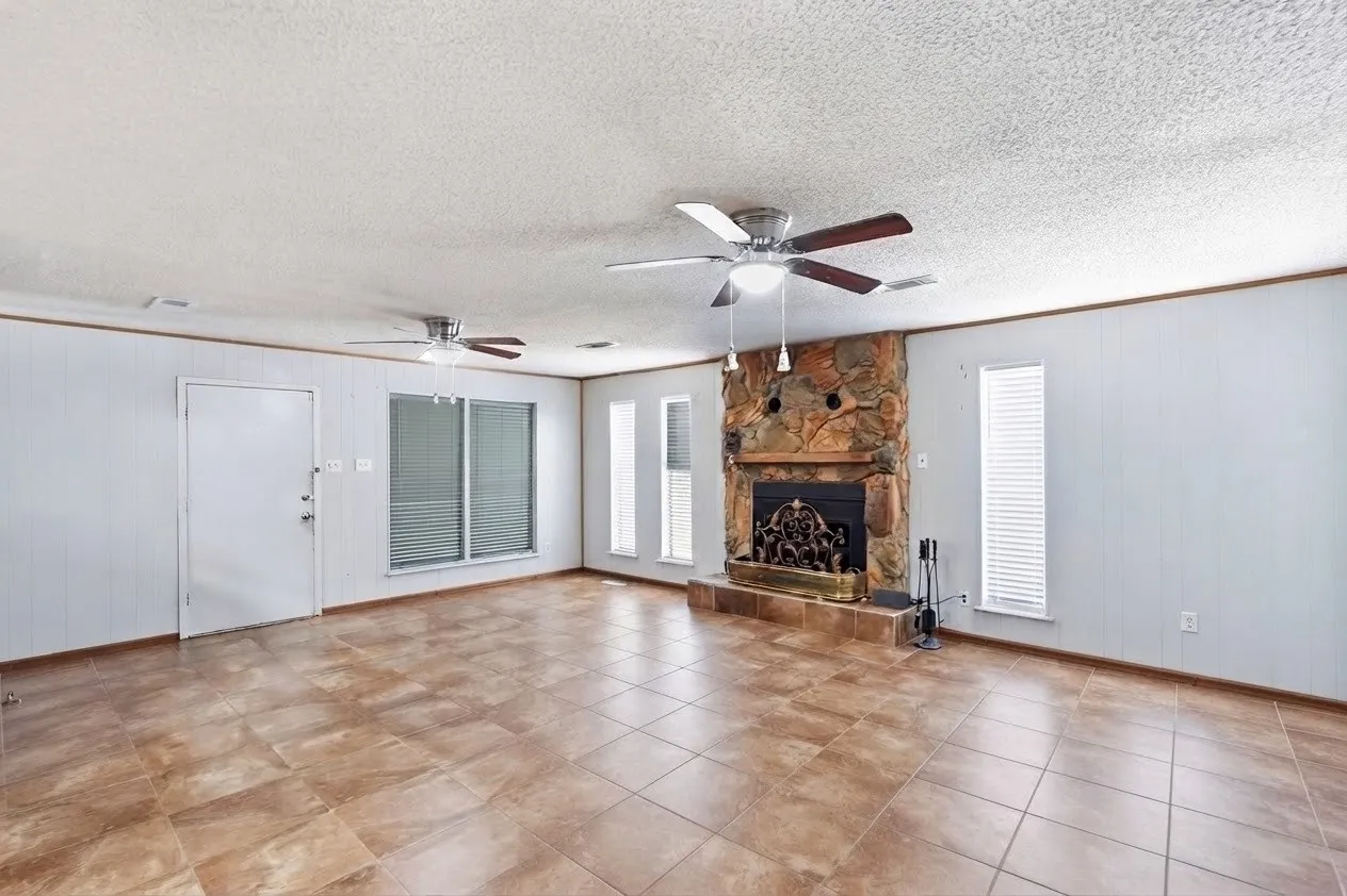Spacious room featuring tile flooring, a stone-clad fireplace, and multiple windows for natural light