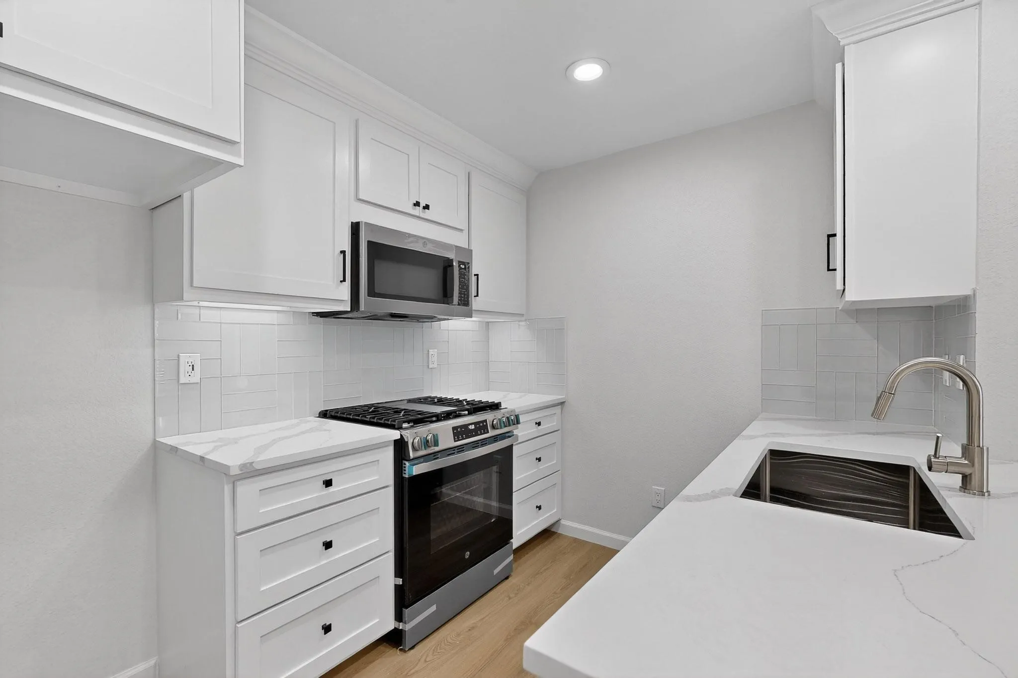 White shaker-style cabinetry, quartz countertops, stainless steel appliances, tile backsplash, and a stainless steel sink with a gooseneck faucet