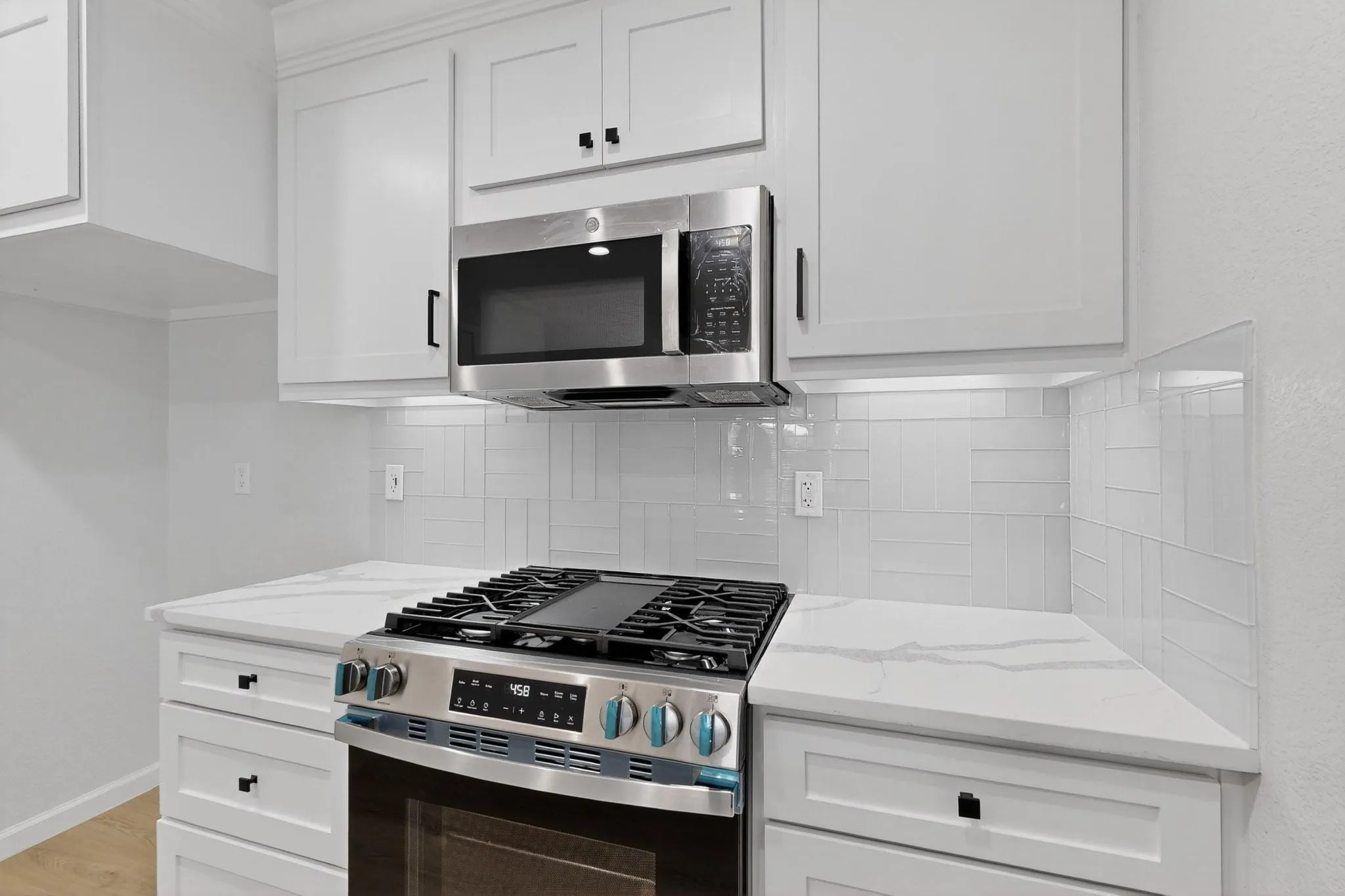 Stainless steel range with a built-in microwave, white shaker-style cabinetry with matte black hardware, quartz countertops, and a white subway tile backsplash