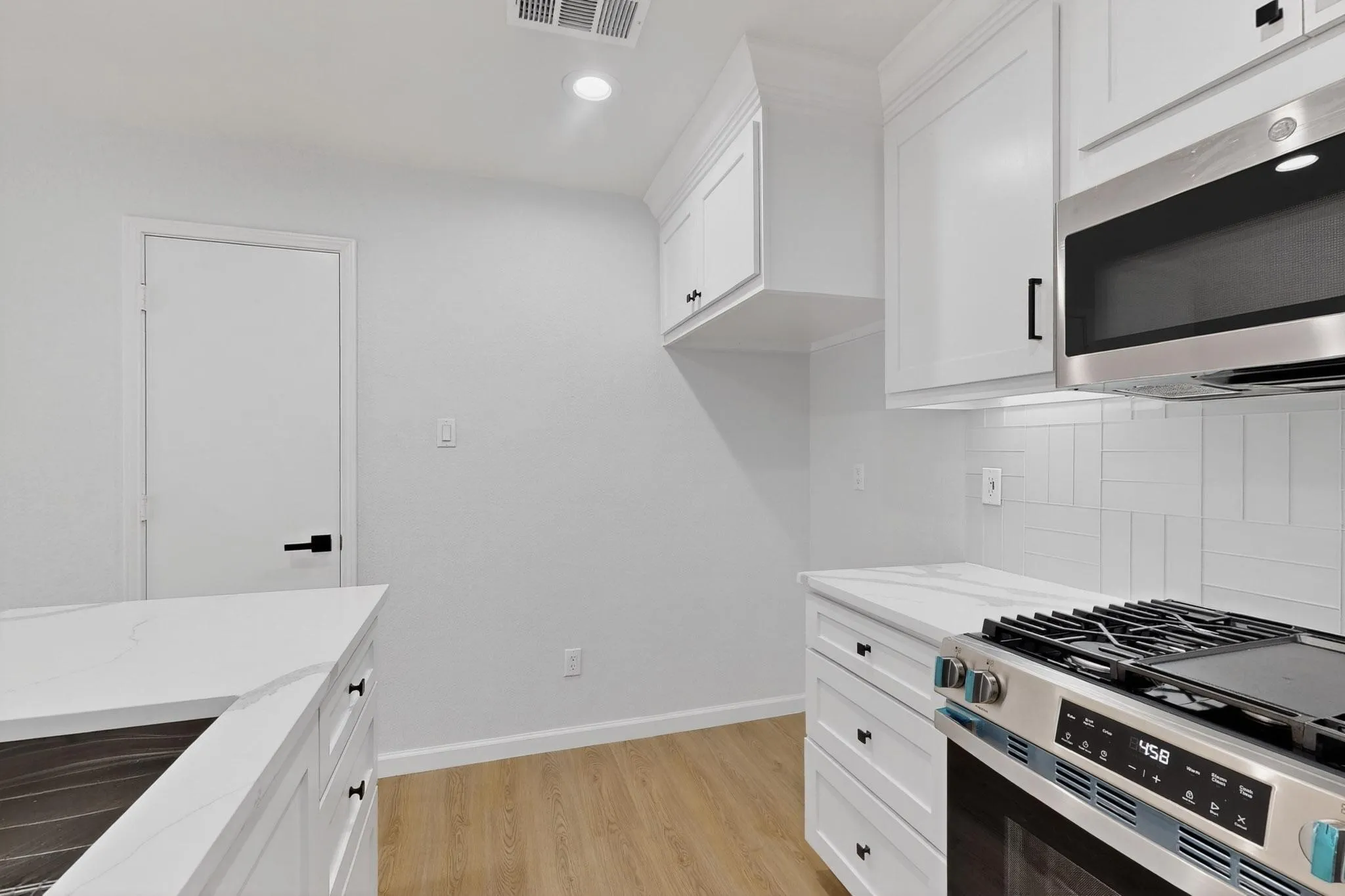 White shaker cabinetry, light wood-finish flooring, stainless steel appliances, white subway tile backsplash, and white countertops