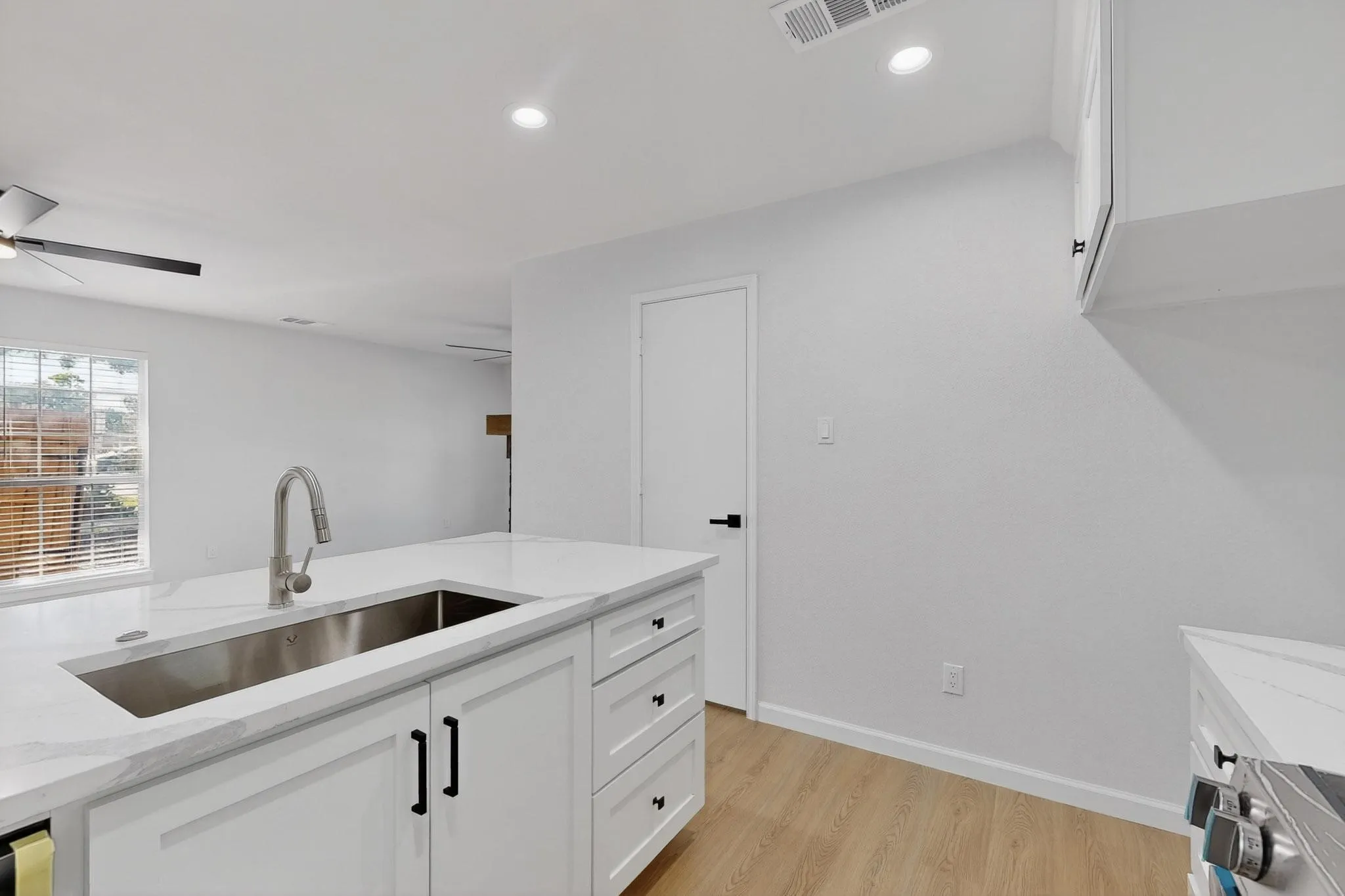 Kitchen island with an undermount stainless steel sink, a pull-down faucet, white shaker cabinetry, and light-toned wood-finish flooring