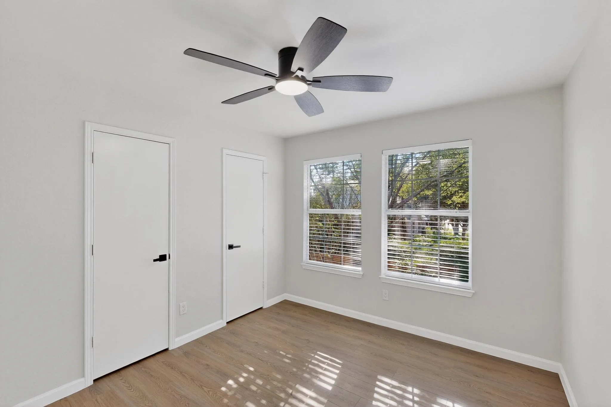 Recessed lighting, wood-finish flooring, two windows with blinds, two interior doors, and a ceiling fan with light