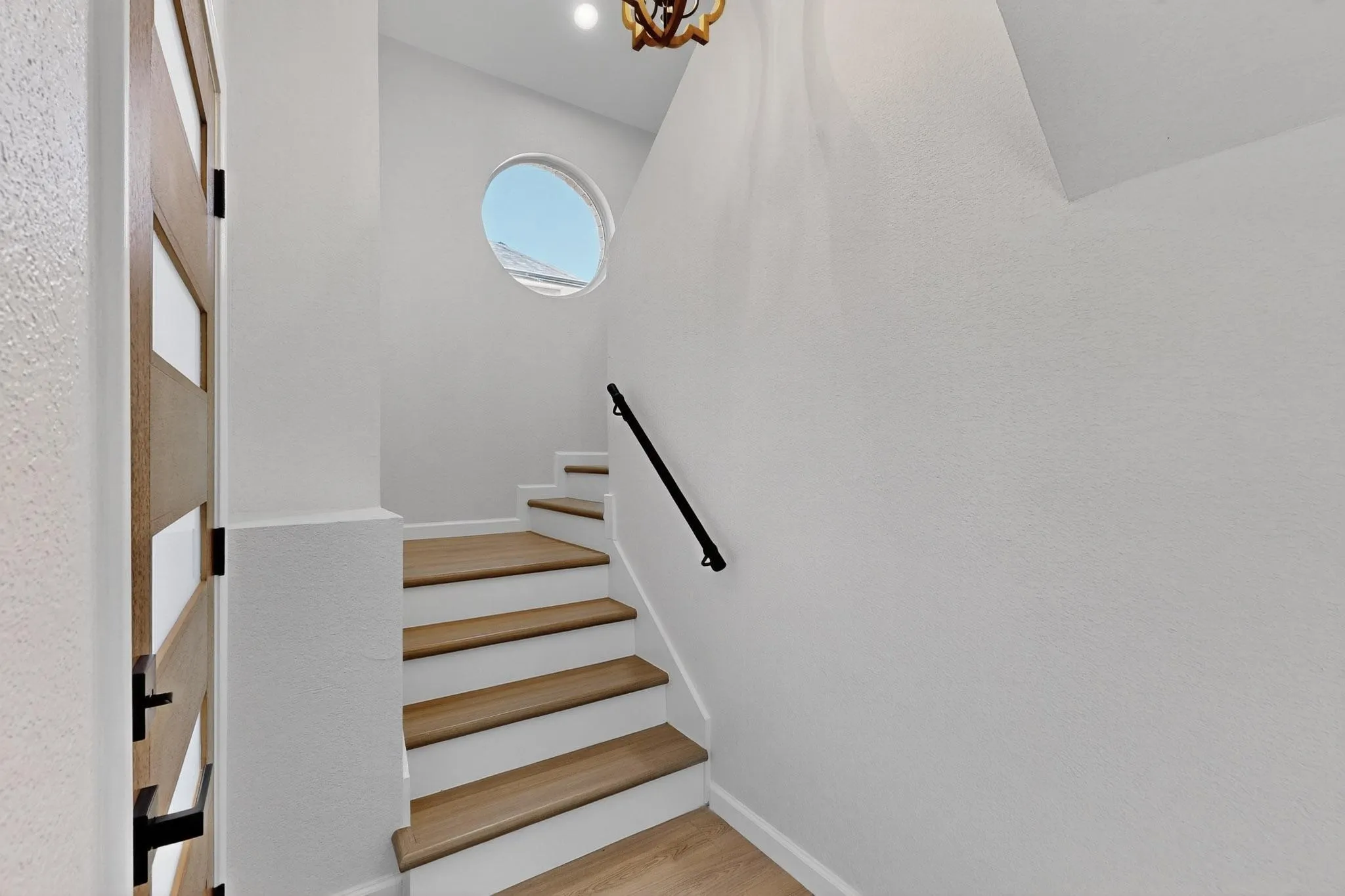 Wood-finish staircase treads with white risers, a circular window, and a modern black handrail