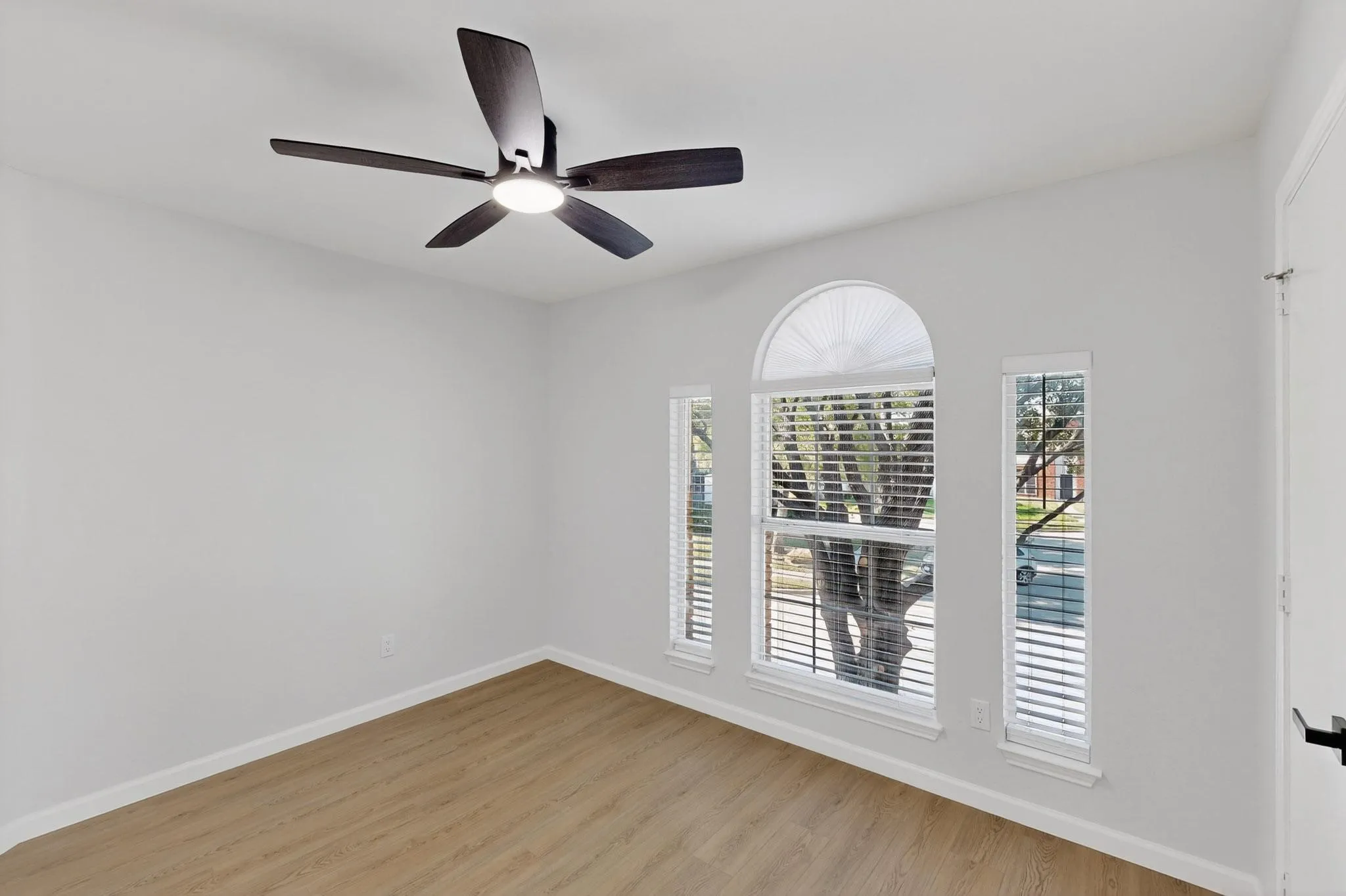 Wood-finish flooring, contemporary ceiling fan with integrated lighting, and multiple windows with an arched transom