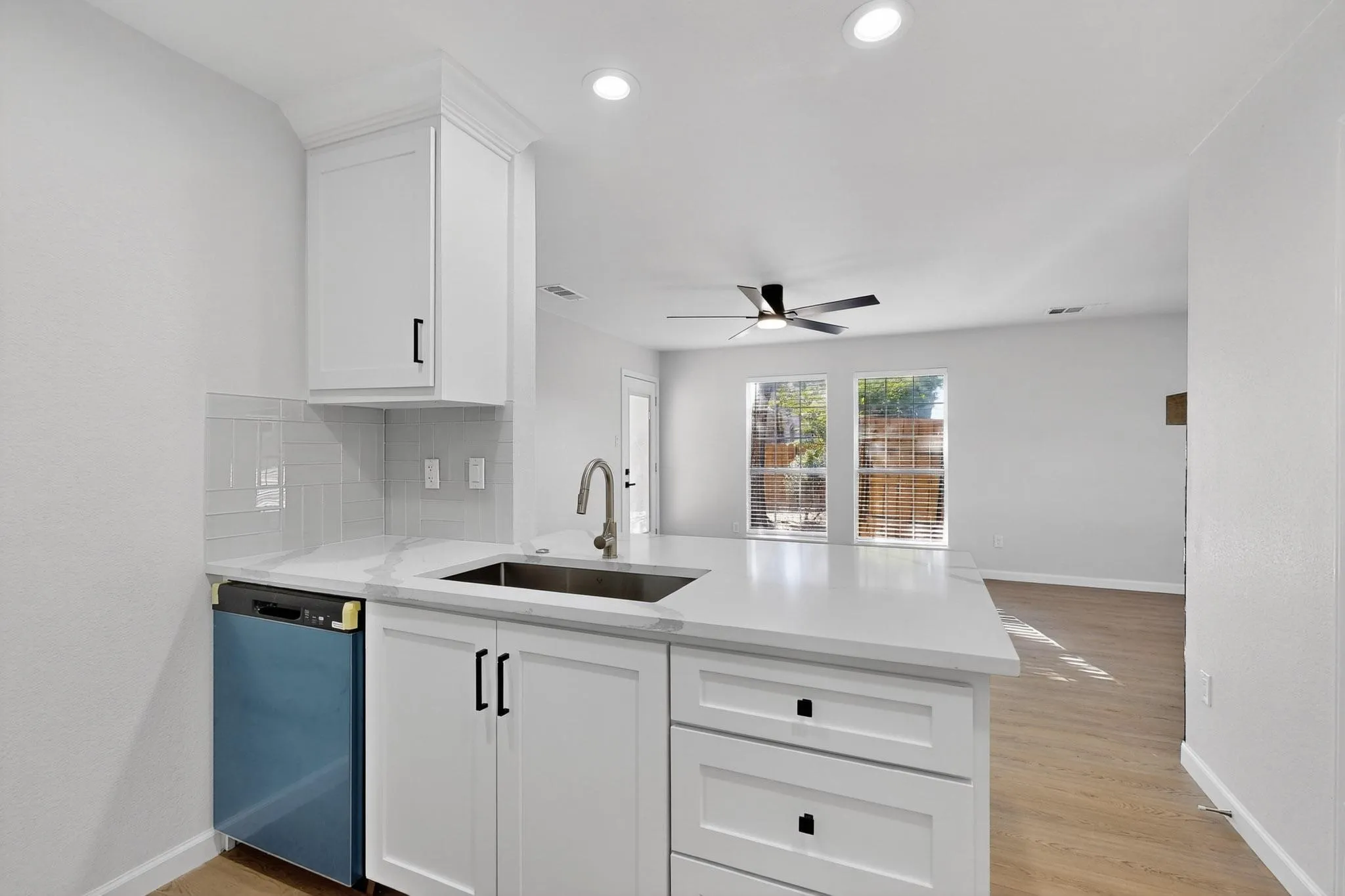 Kitchen featuring white shaker cabinetry, light-toned countertops, a stainless steel sink with a gooseneck faucet, and a subway tile backsplash
