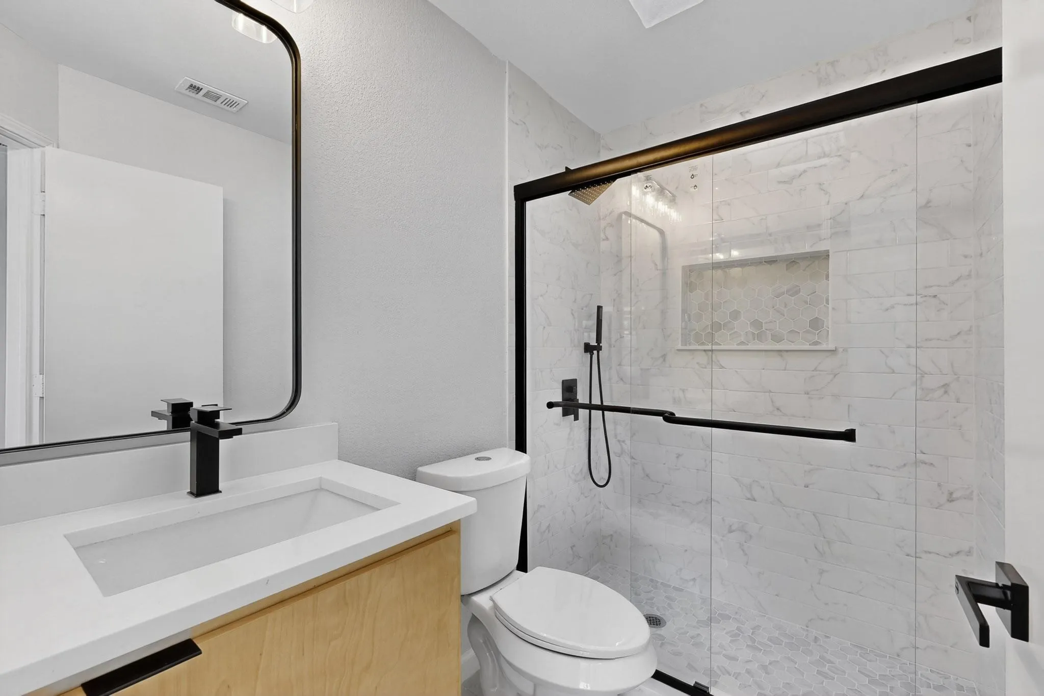 Contemporary bathroom featuring a light wood-finish vanity with an integrated sink, black-framed mirror, and matte black fixtures