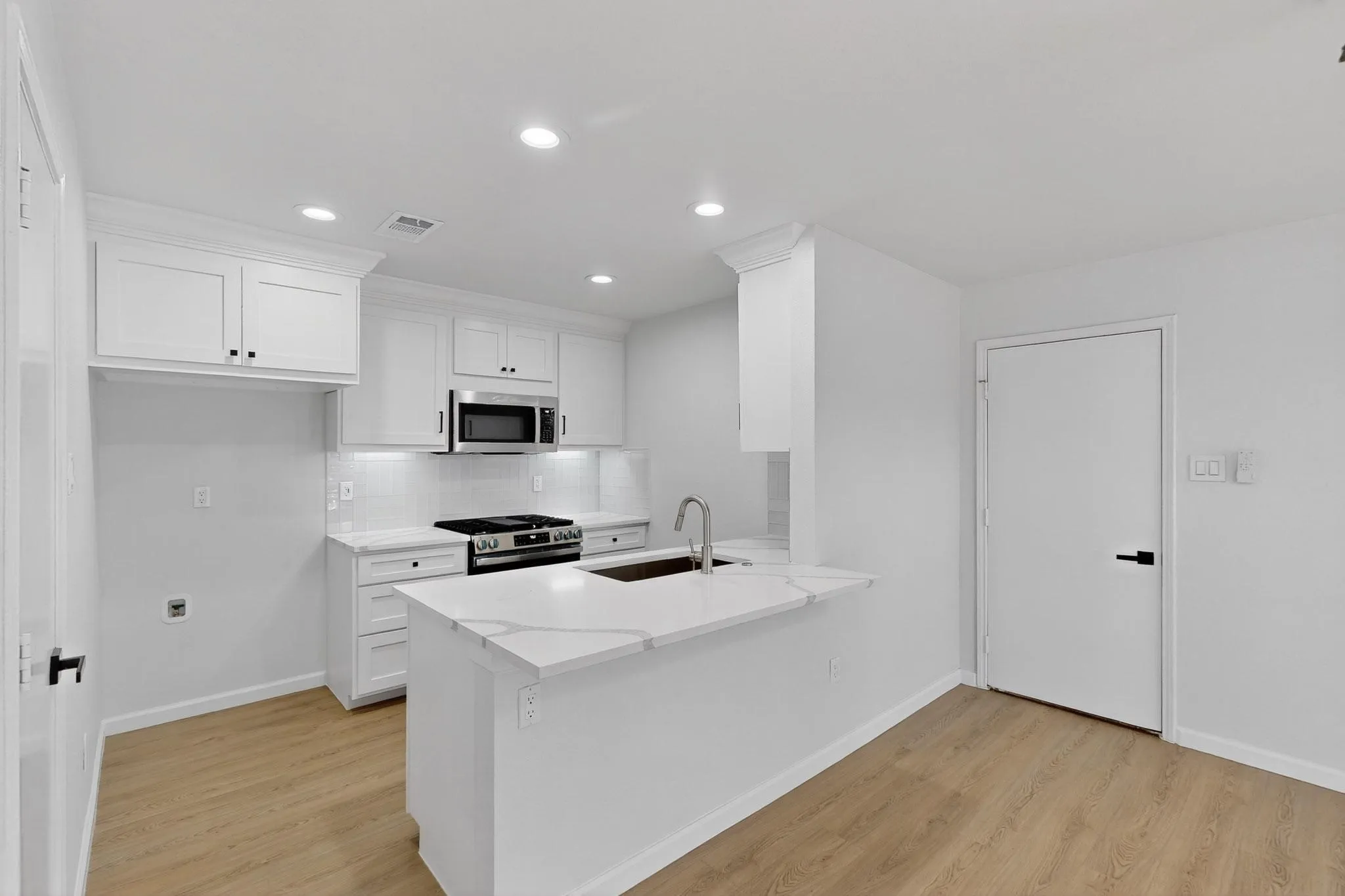 Kitchen featuring white cabinetry, stainless steel appliances, a center island with a sink, white countertops, and wood-finish flooring
