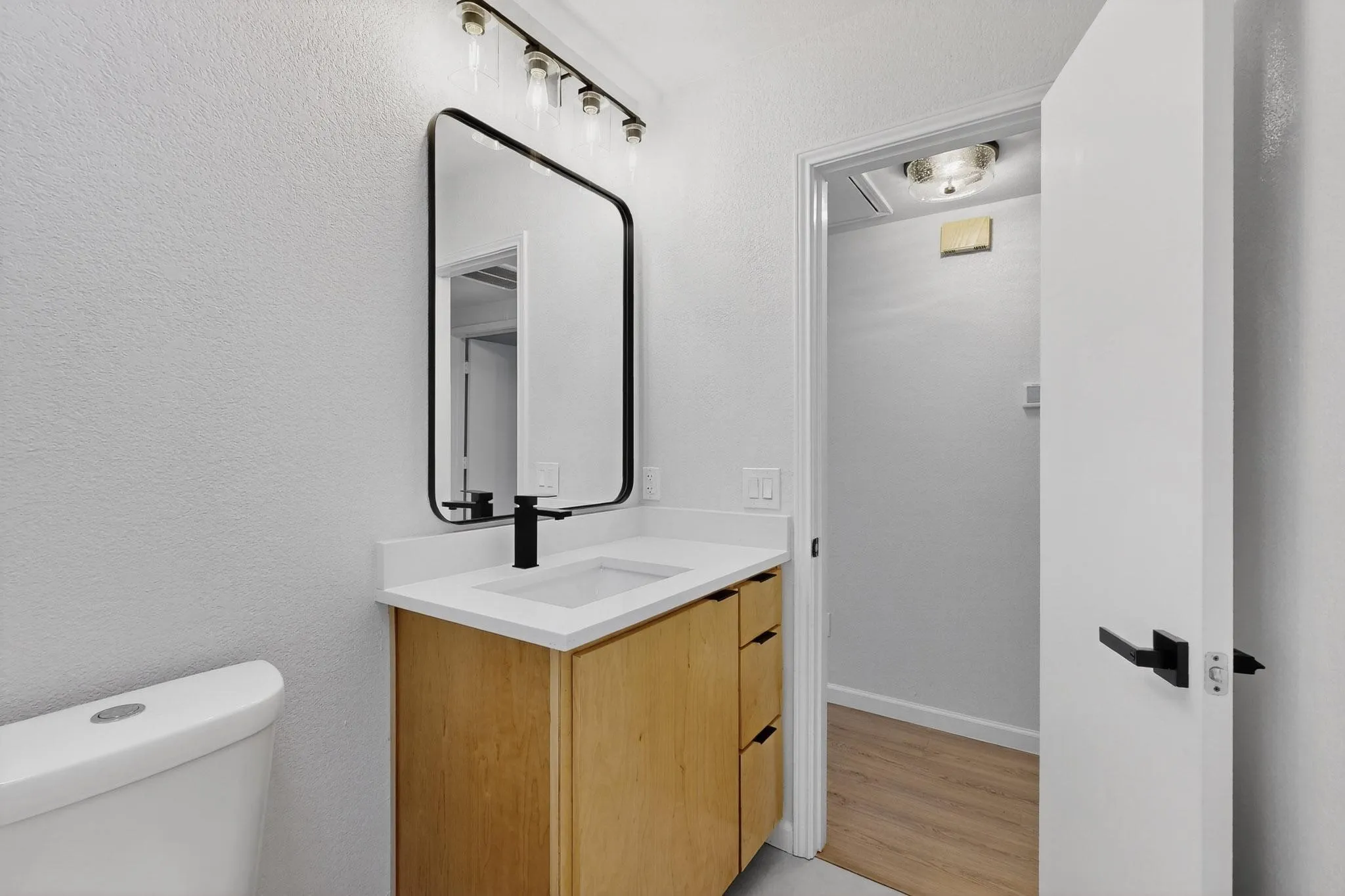 Bathroom featuring a wood-finish vanity with a white countertop, rectangular basin, and matte black faucet