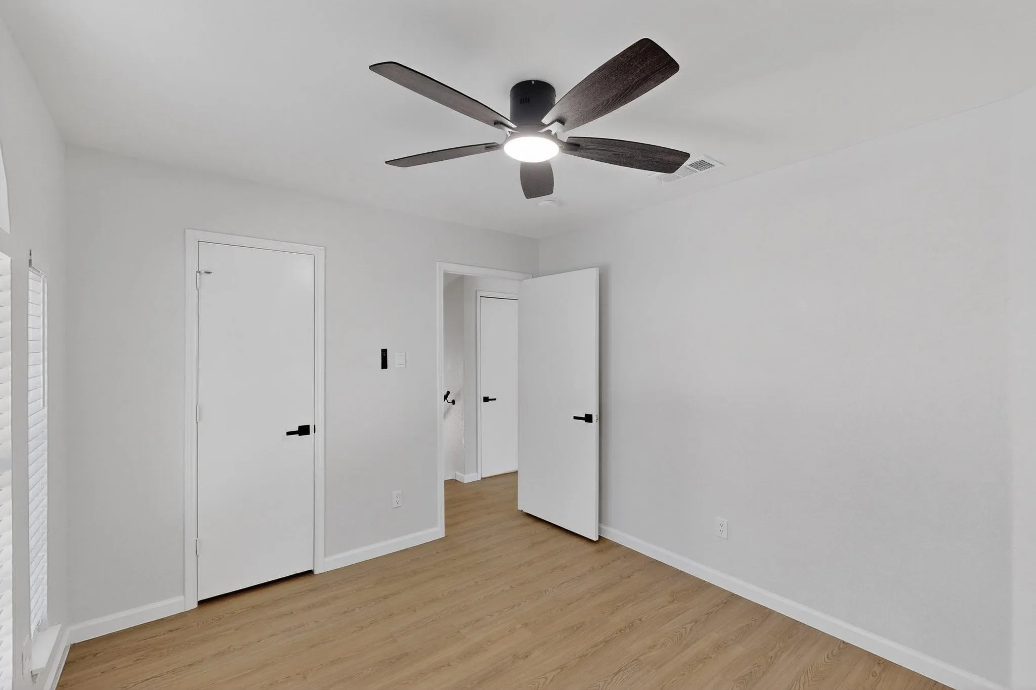Wood-finish flooring, white walls, white doors with matte black hardware, and a ceiling fan with integrated lighting