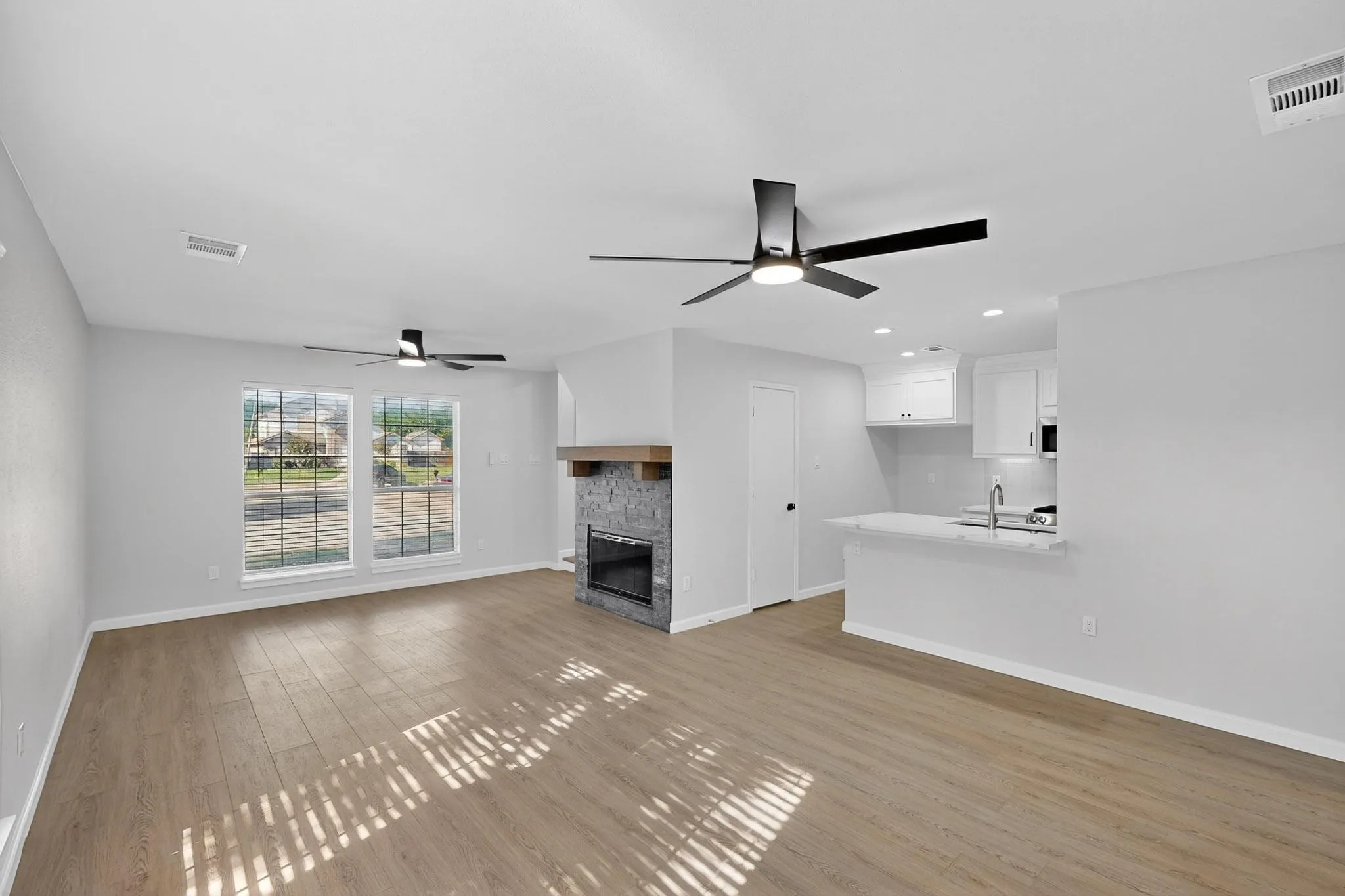 Open-concept living space with wood-finish flooring, a stone-surround fireplace with a wood mantle, and a kitchen island with a built-in sink