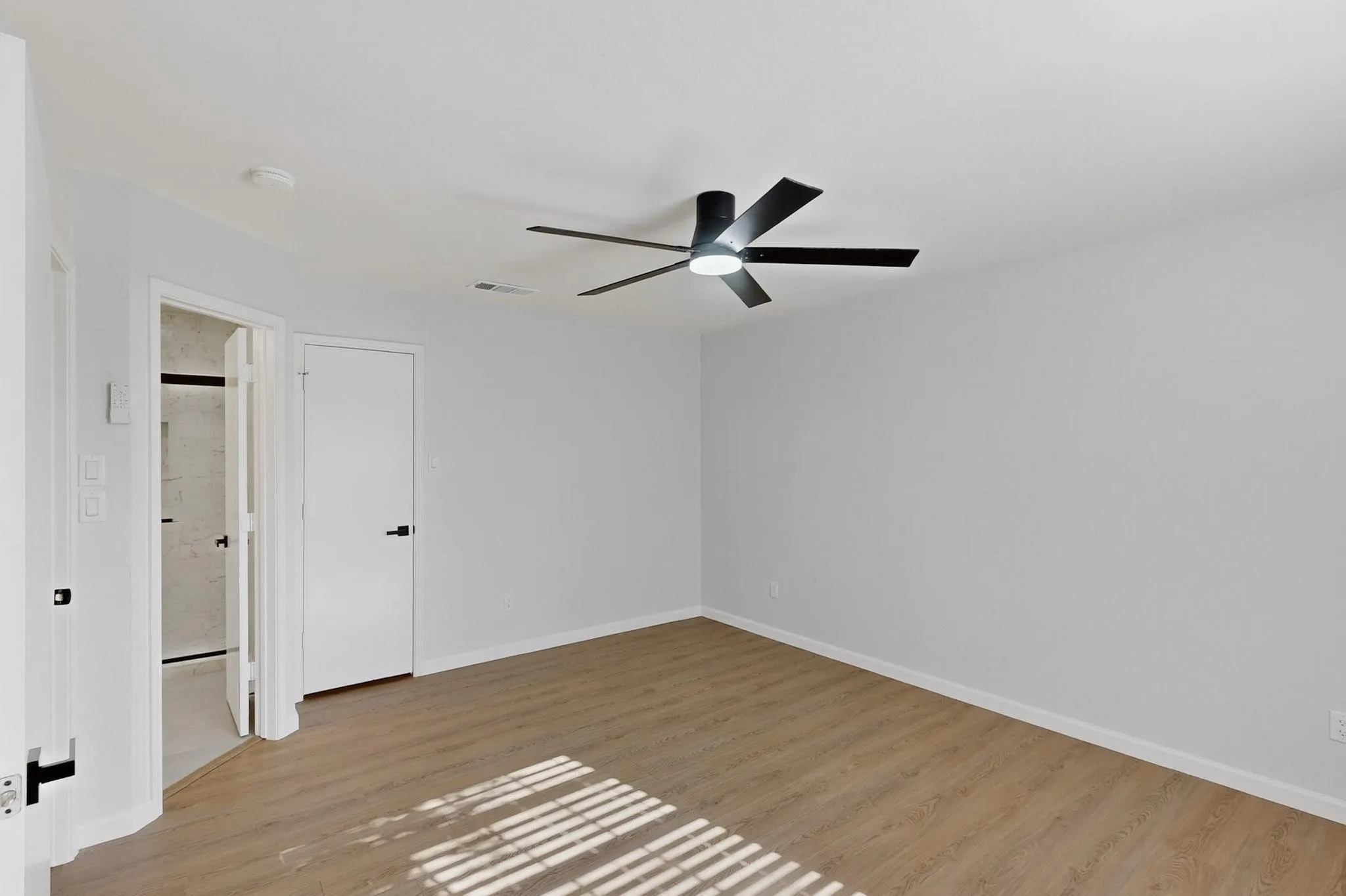 Wood-finish flooring with white walls and a modern black ceiling fan