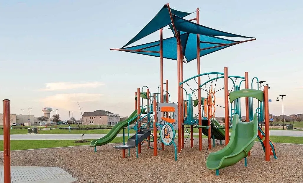 Community playground featuring multiple slides, climbing structures, and shade canopies over wood chip surfacing
