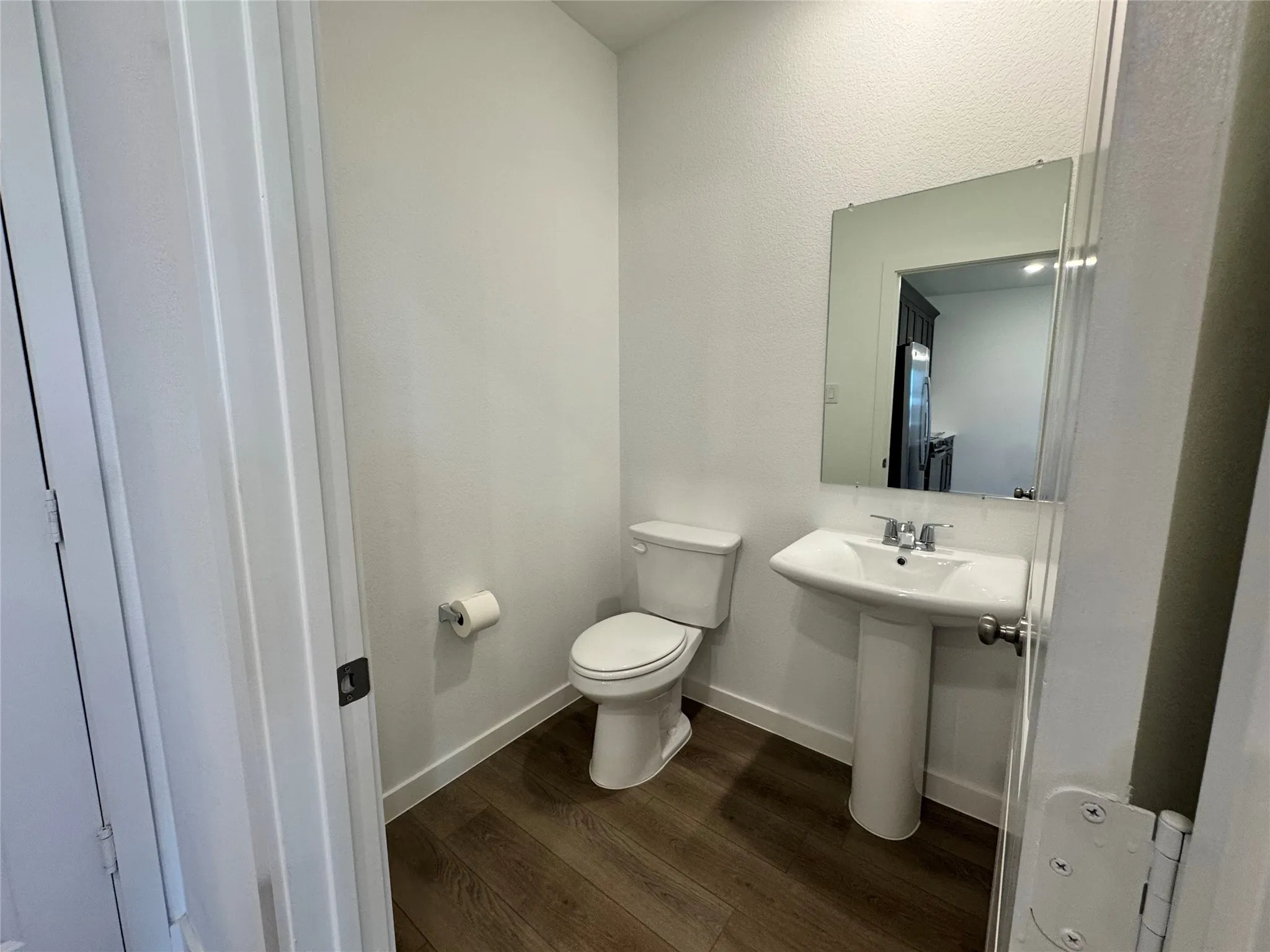 Pedestal sink with chrome faucet, a rectangular mirror, and wood-finish flooring
