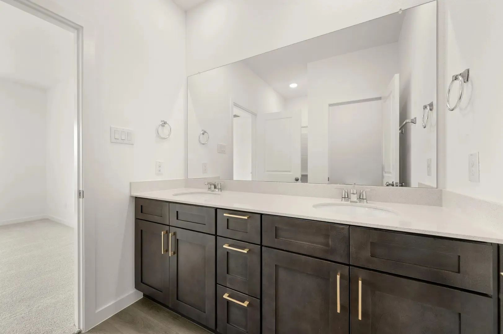 Double vanity with dark wood-finish cabinetry, gold-tone hardware, and an expansive mirror