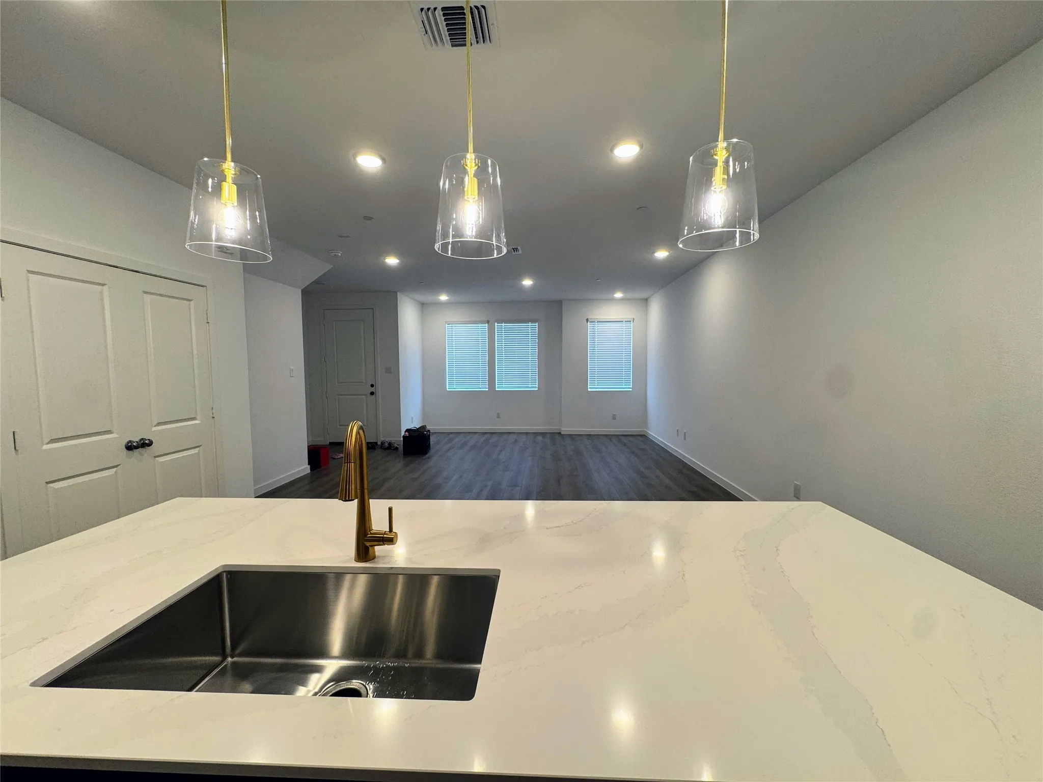 Kitchen island featuring a single-basin undermount sink with a gold-tone faucet, white countertop, and three pendant lights