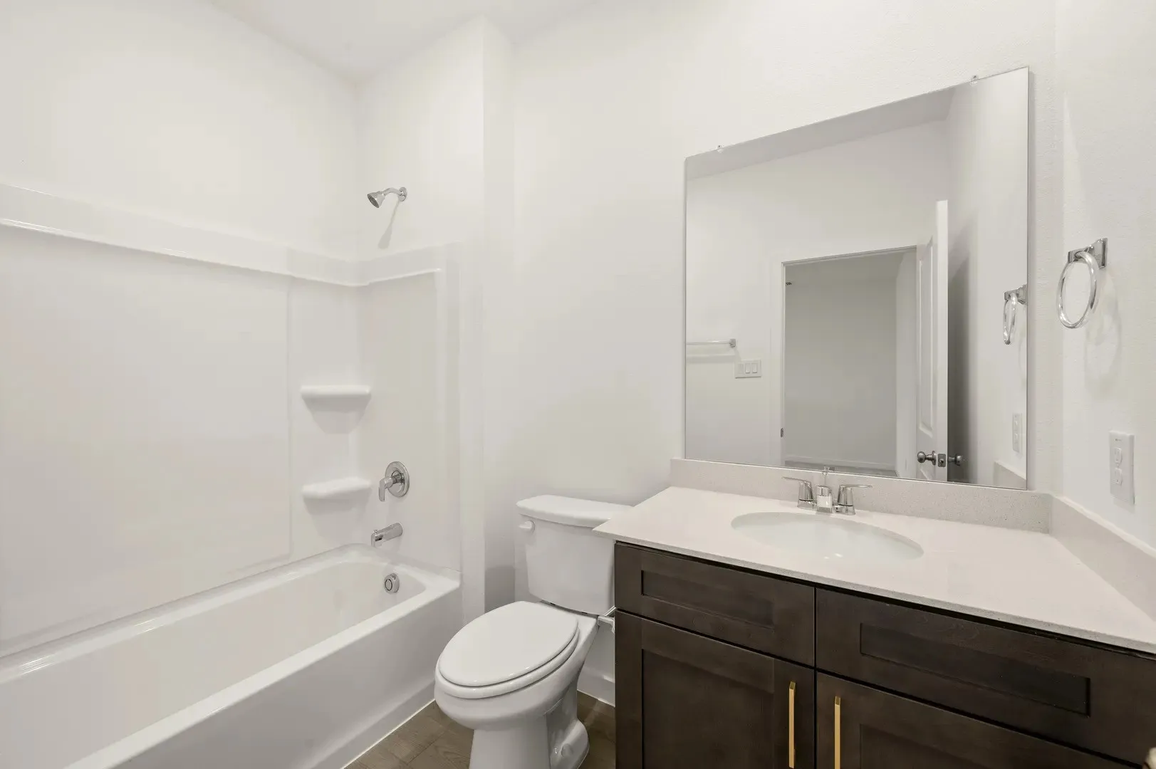 Bathroom featuring a shower-tub combination with a white surround, a toilet, and a vanity with dark wood-finish cabinetry, a light-toned countertop, and an undermount sink