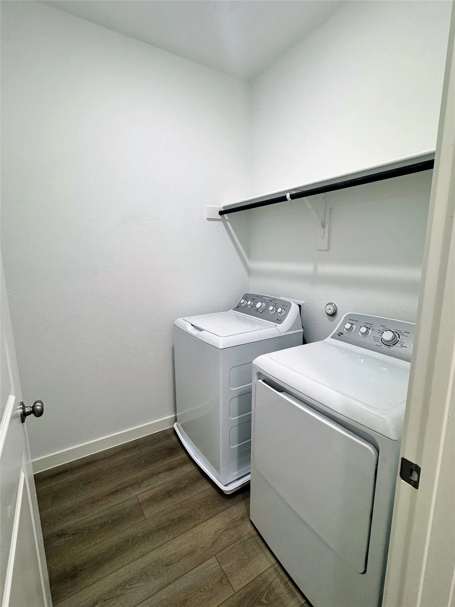 Dedicated laundry area featuring wood-finish flooring, white walls, a built-in shelf, and a hanging rod