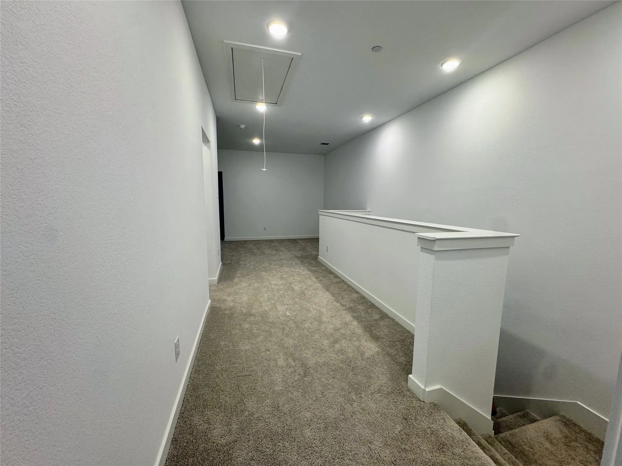 Upper level landing featuring neutral carpeting, recessed lighting, white walls, and a staircase with a white railing