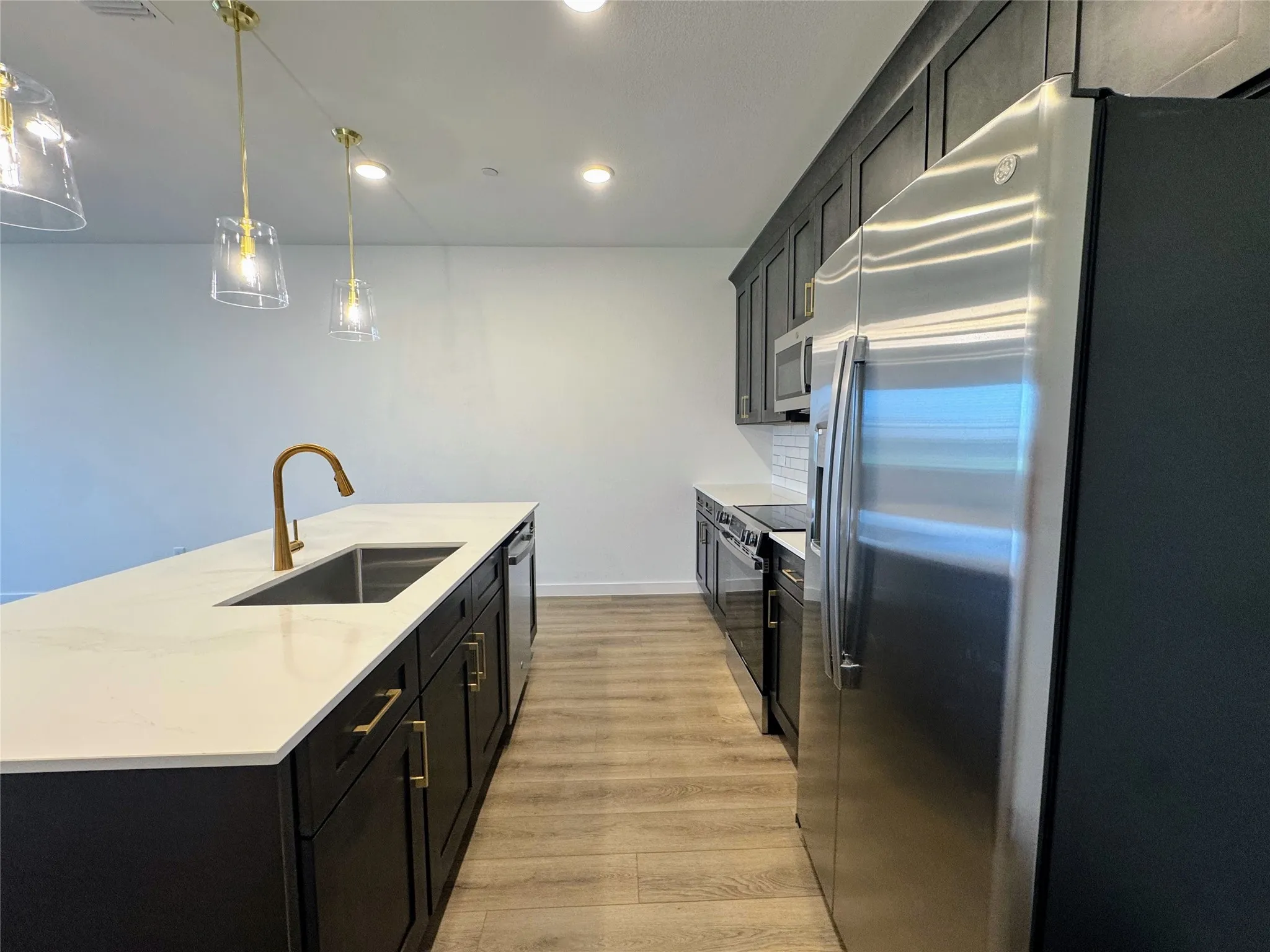 Kitchen featuring a large island with a stainless steel sink and a gold-tone faucet, complemented by white countertops