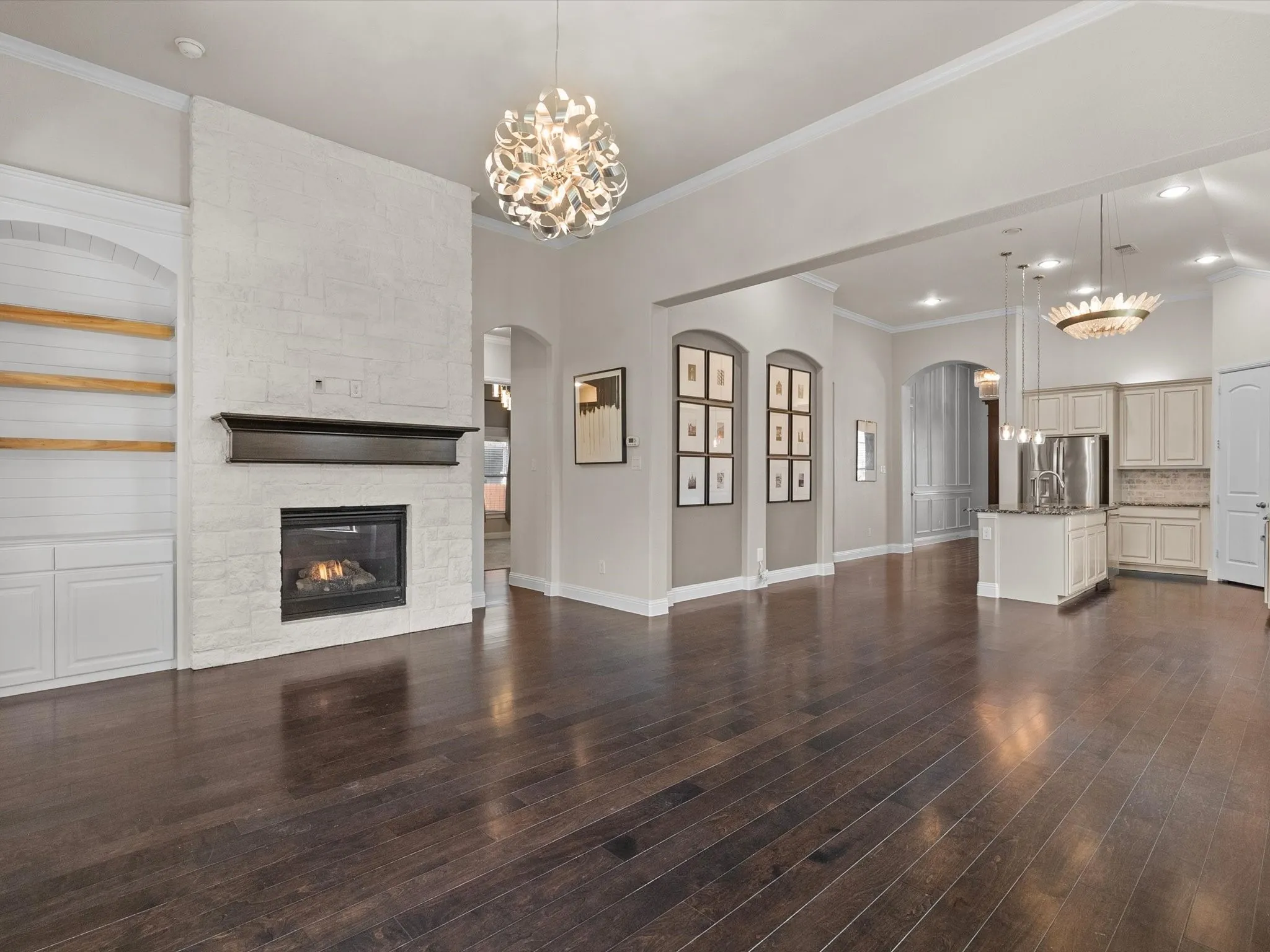 Expansive open-concept space with dark wood-finish flooring, a brick-textured fireplace with a mantel, and built-in cabinetry with open shelving