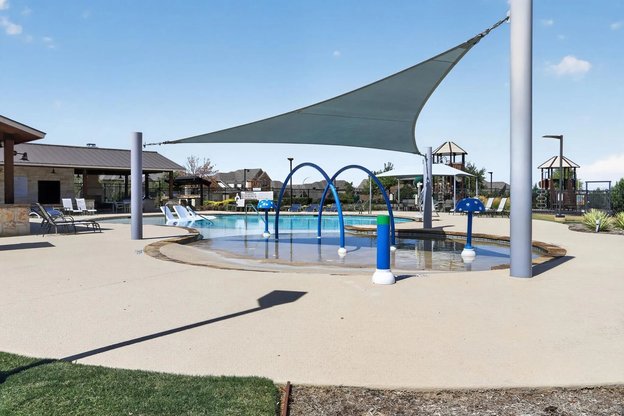 Outdoor pool with a splash pad, shade sail, and surrounding concrete deck