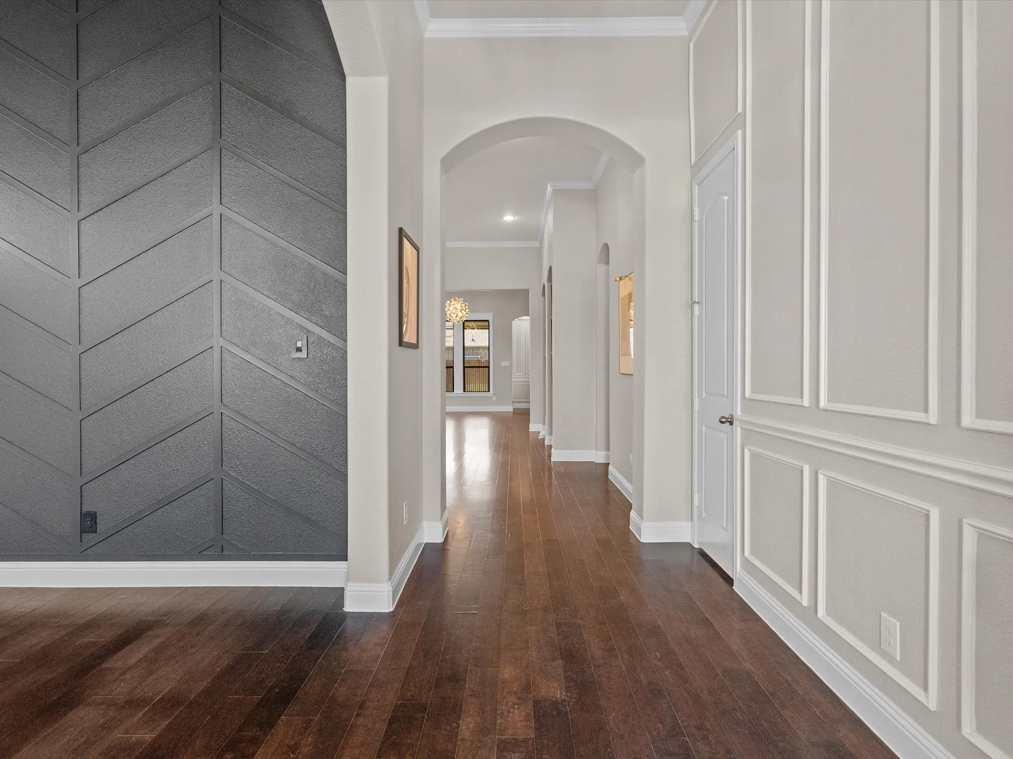 Hardwood flooring, decorative wall paneling, crown molding, arched doorways, and built-in lighting