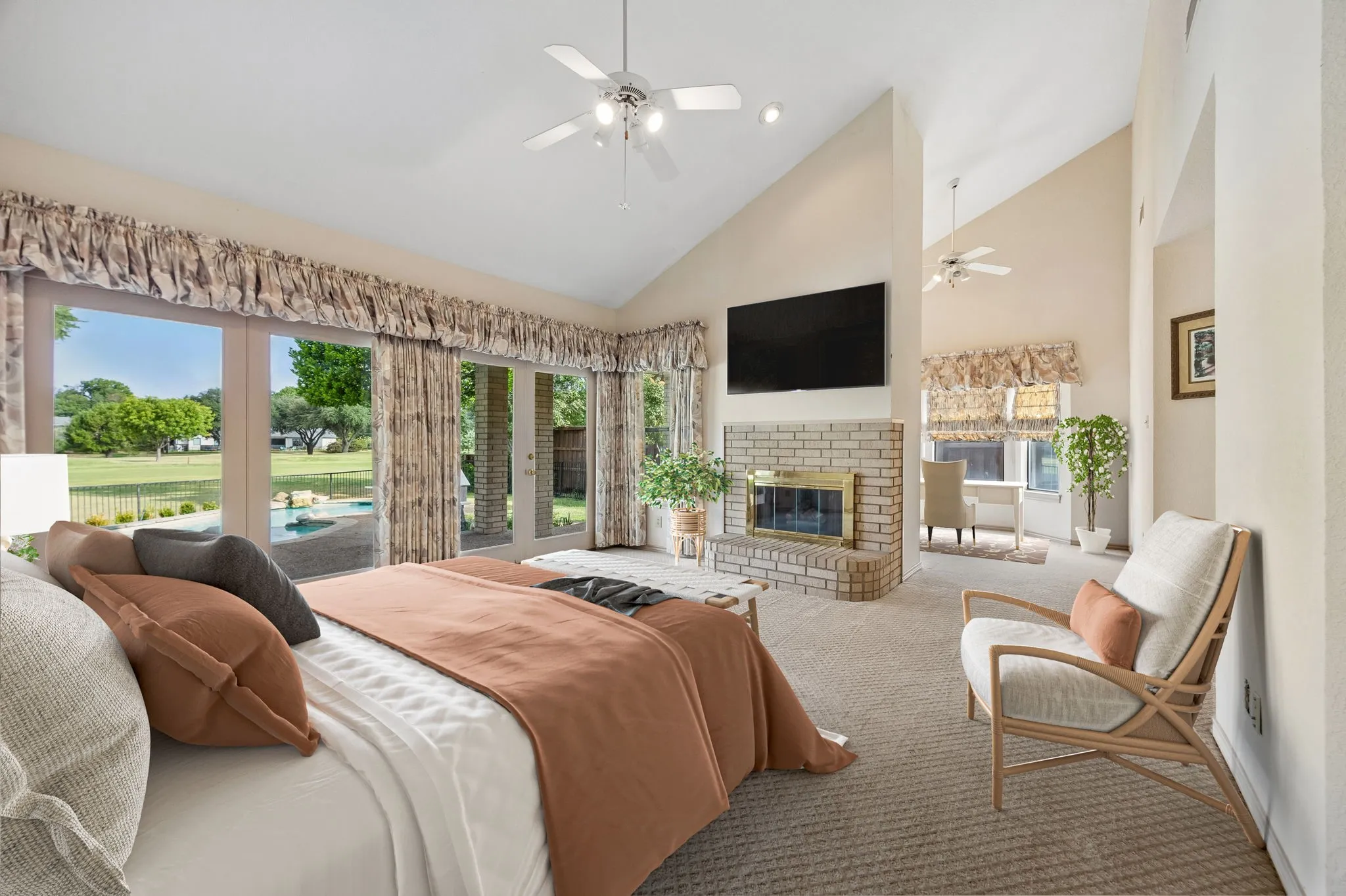 Vaulted ceilings, brick fireplace, wall-mounted television, and expansive glass doors leading to the exterior