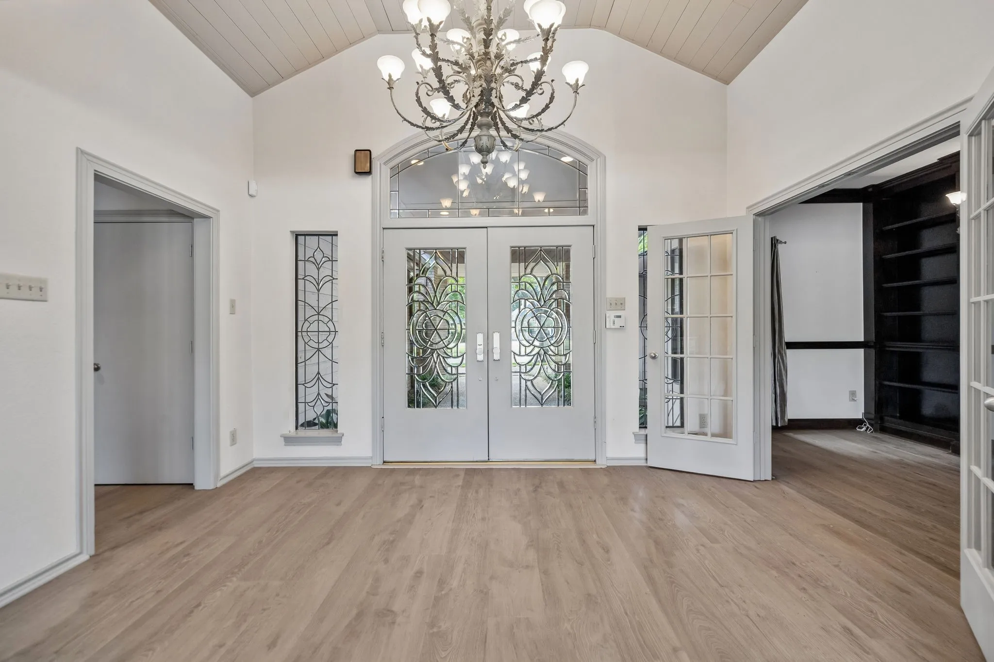 Vaulted ceiling entryway with wood-finish flooring, an ornate chandelier, and double doors featuring decorative glass inserts