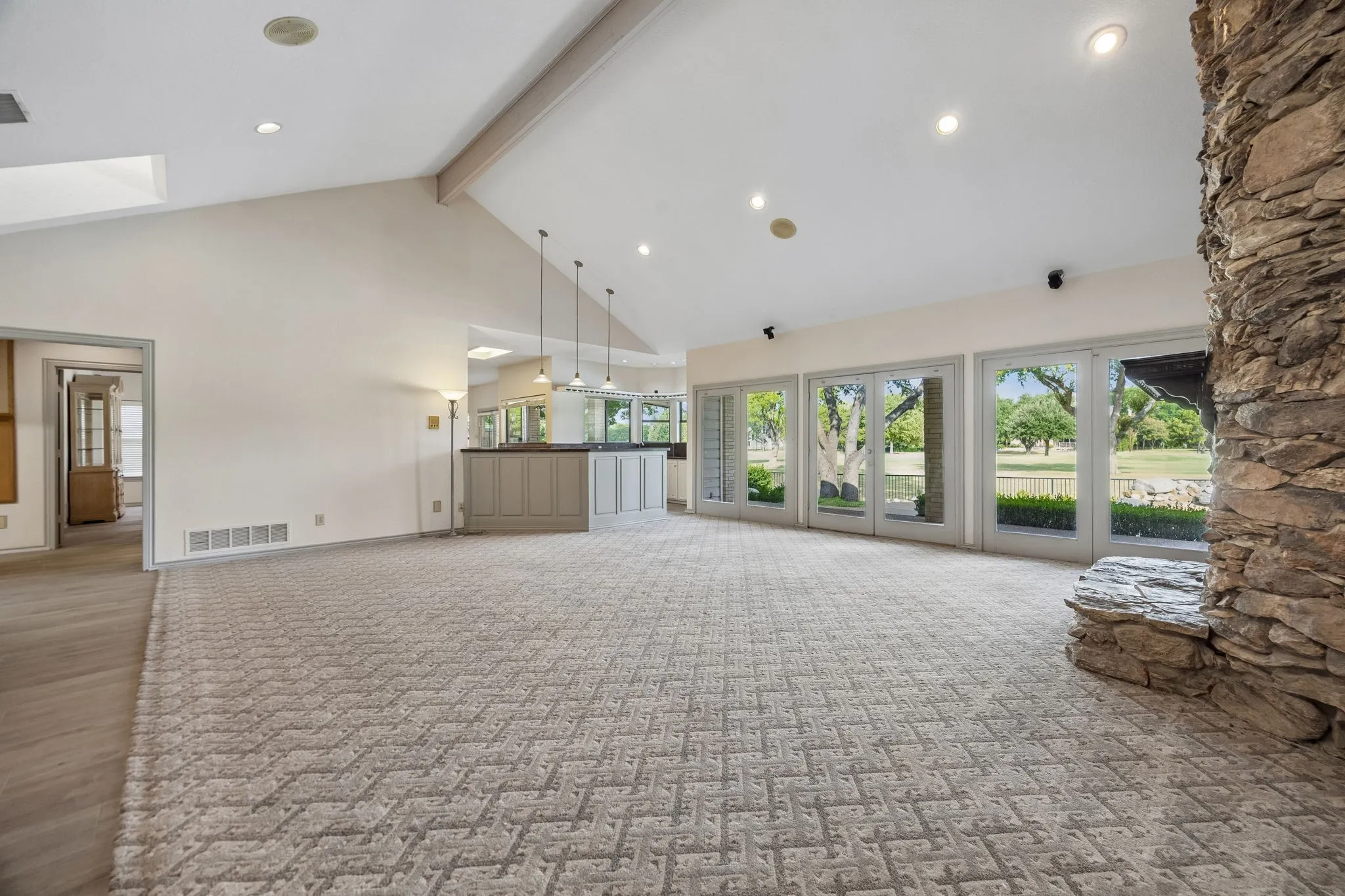 Vaulted ceiling with recessed lighting, stone fireplace, multiple glass panel doors, and a built-in bar with pendant lighting