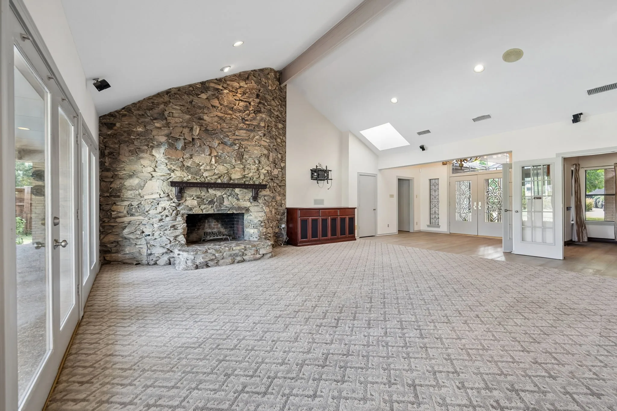 Vaulted ceiling with skylight, stone fireplace, recessed lighting, and multiple sets of French doors
