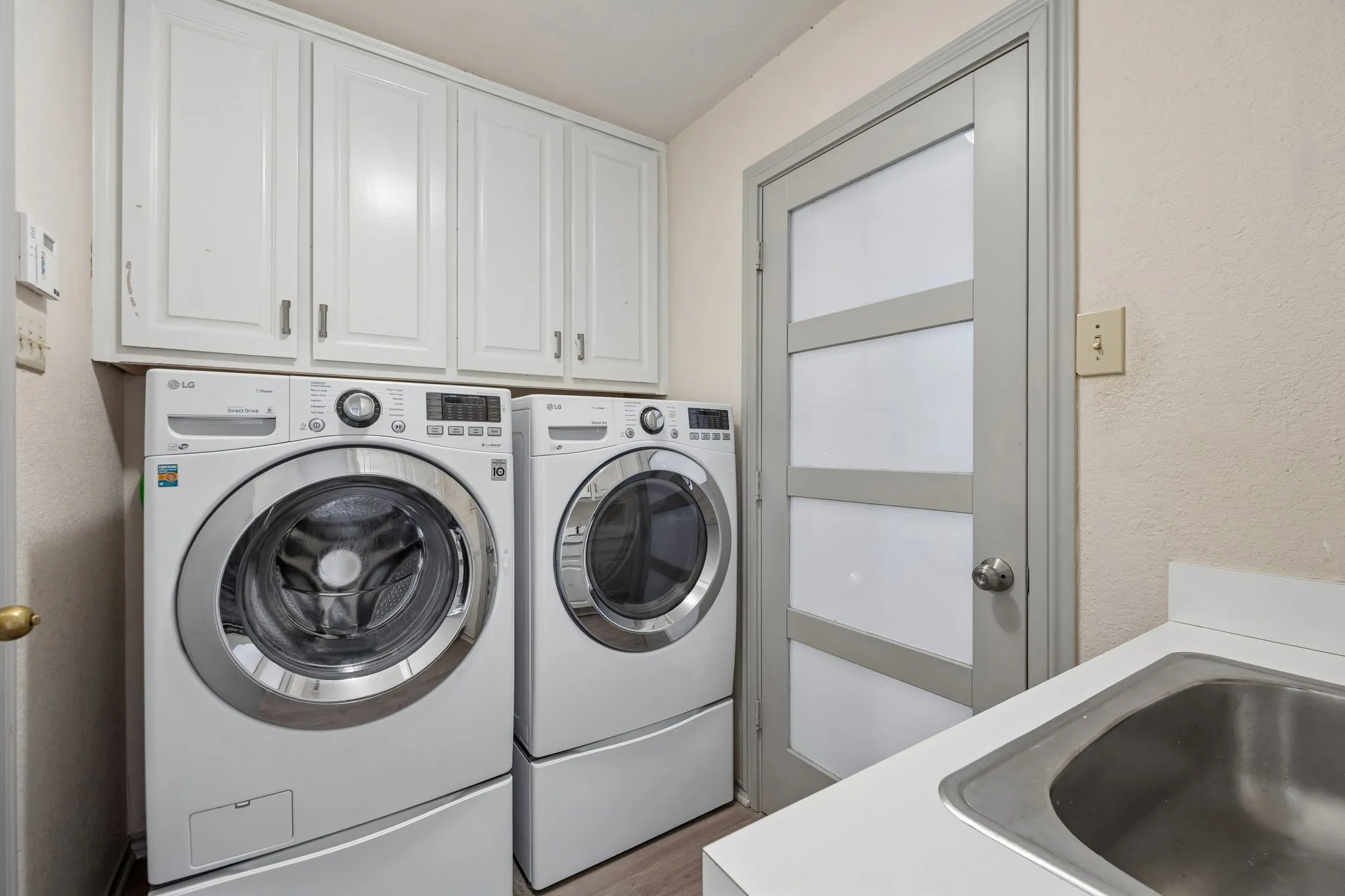 White cabinetry, built-in stainless steel sink, light countertops, light-colored walls, and a modern paneled door