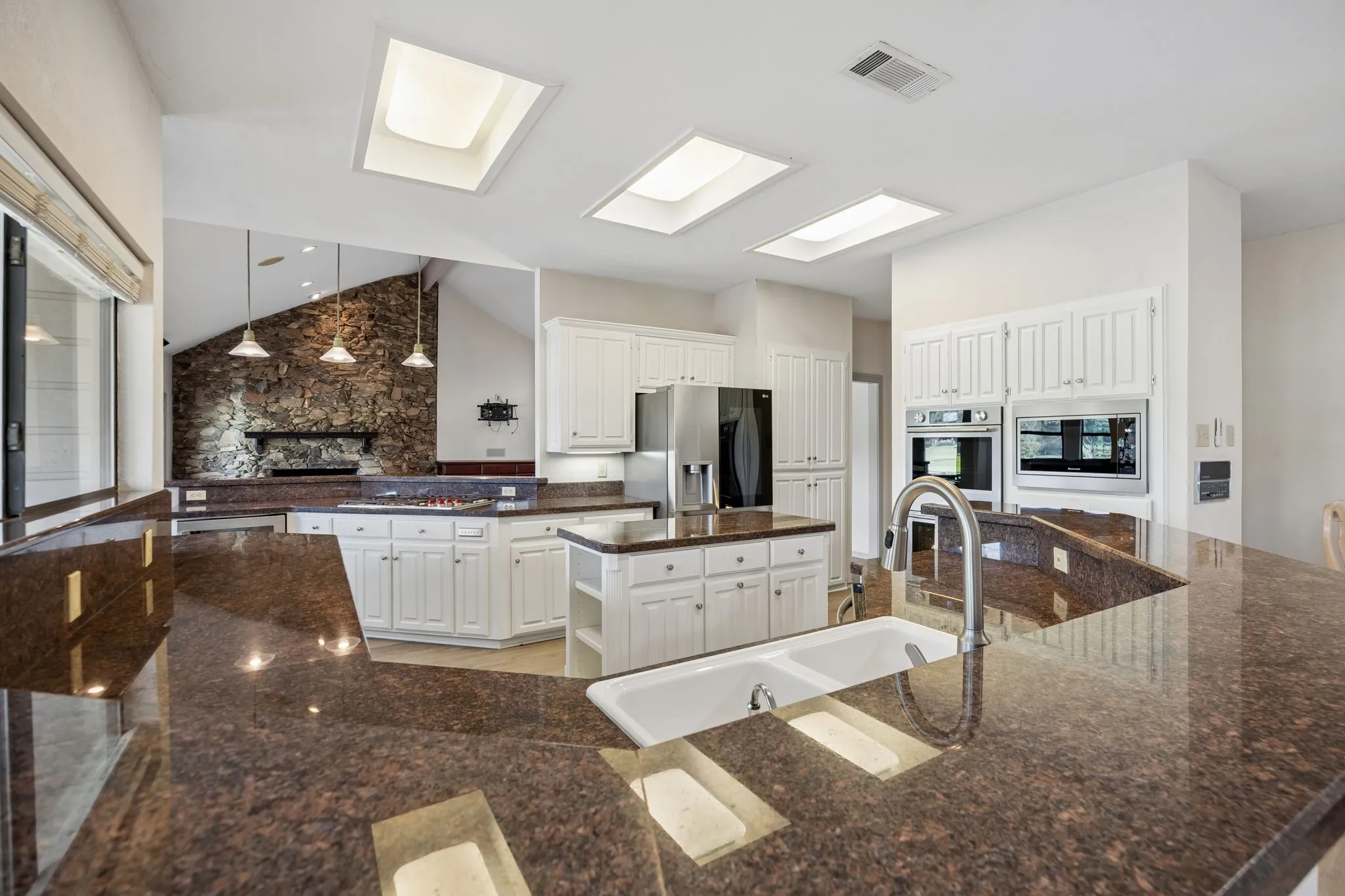 Spacious kitchen featuring extensive dark granite-finish countertops, white cabinetry, a double basin sink with a high-arch faucet, and multiple skylights