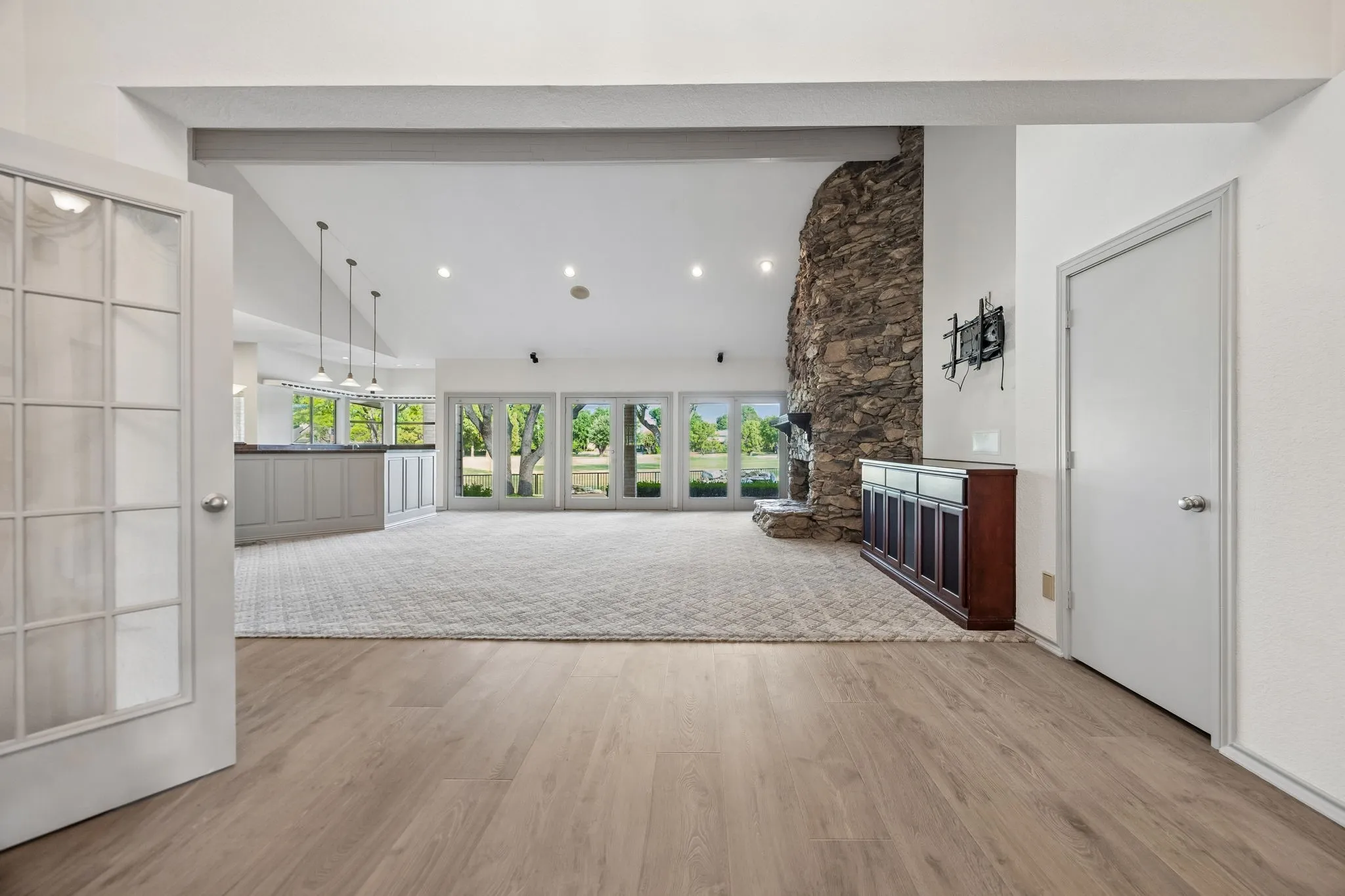 Wood-finish flooring, French doors with frosted glass, stone fireplace, recessed lighting, and expansive windows