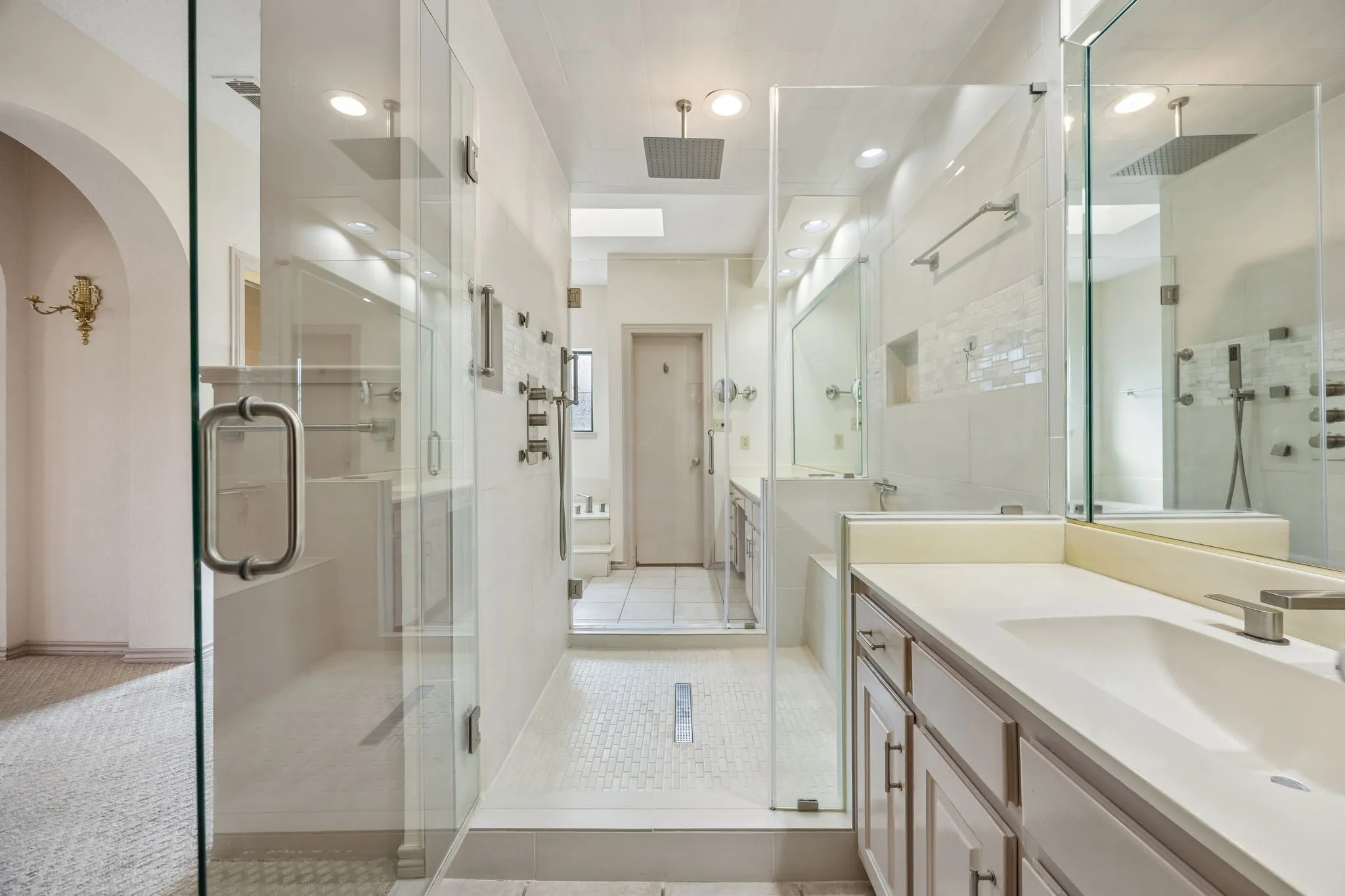 Dual glass-enclosed shower stalls with rainfall showerheads, a double vanity with undermount sinks, and integrated recessed lighting