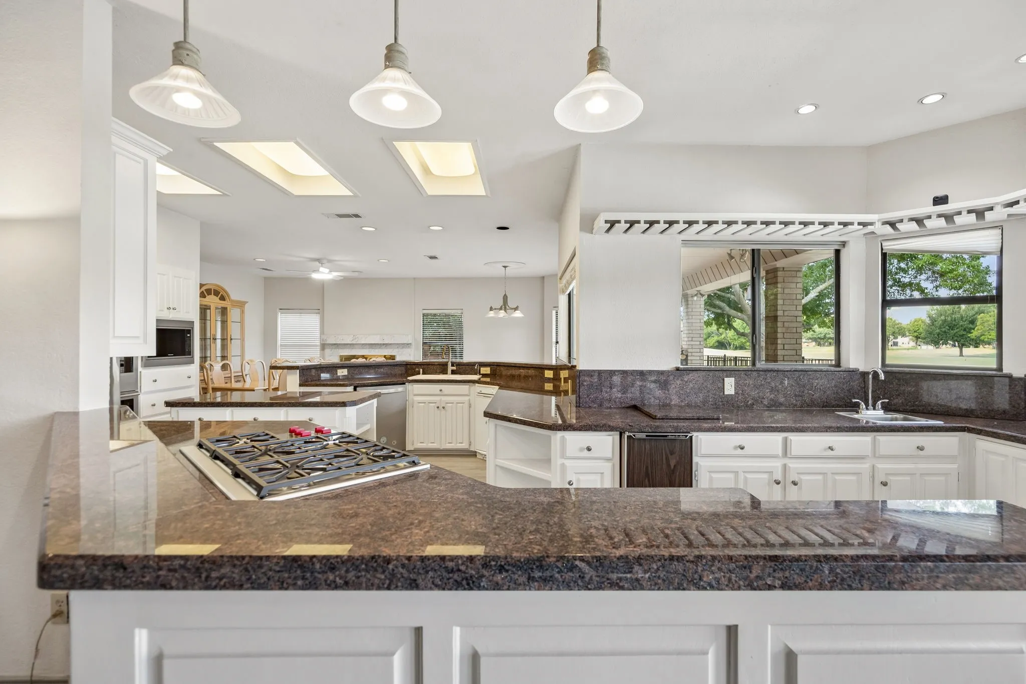 Expansive kitchen featuring white cabinetry, dark stone countertops, a built-in gas cooktop, and multiple skylights
