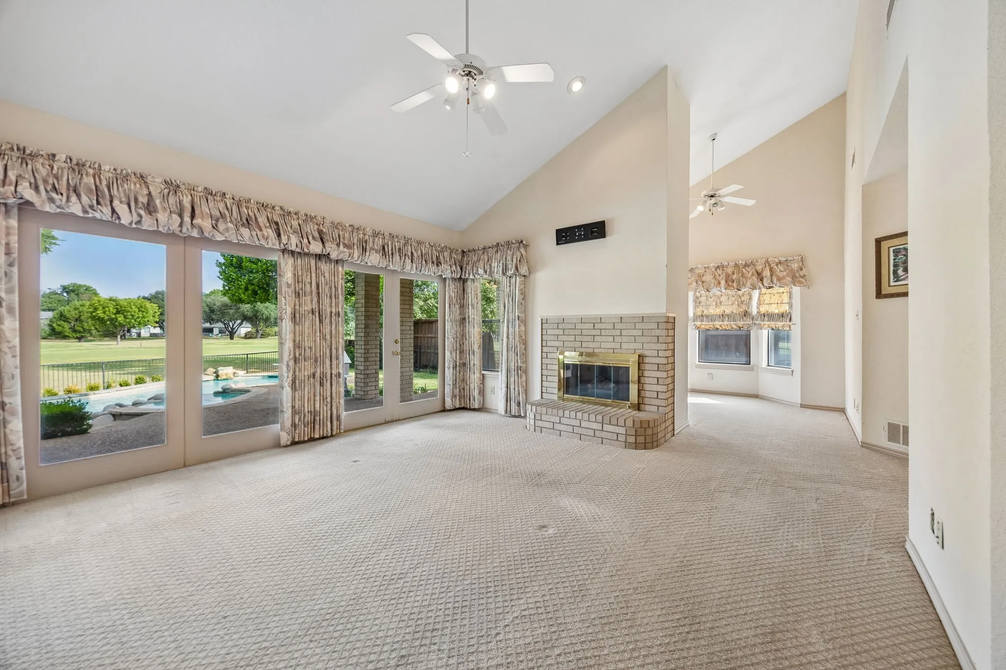 Spacious living area featuring expansive glass doors, vaulted ceilings, a brick-surround fireplace, and light-toned carpeting