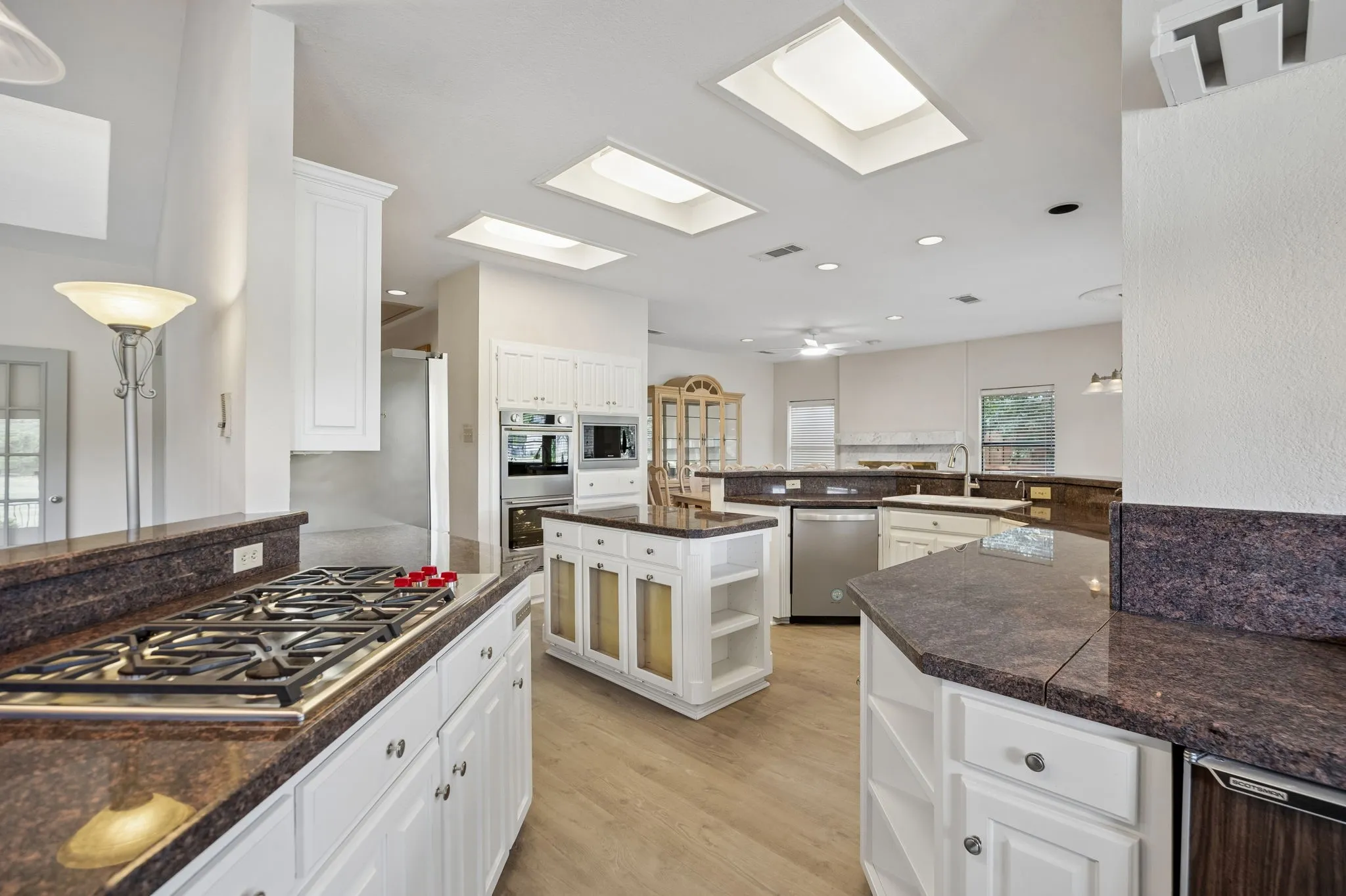 Spacious kitchen featuring multiple skylights, white cabinetry, dark stone countertops, and stainless steel appliances