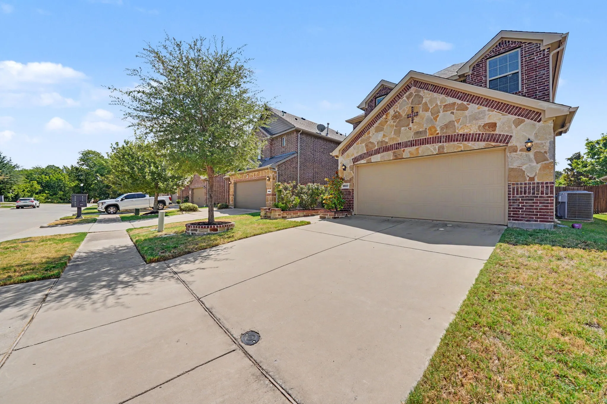 Brick and stone facade, two-car garage, concrete driveway, manicured lawn, established trees