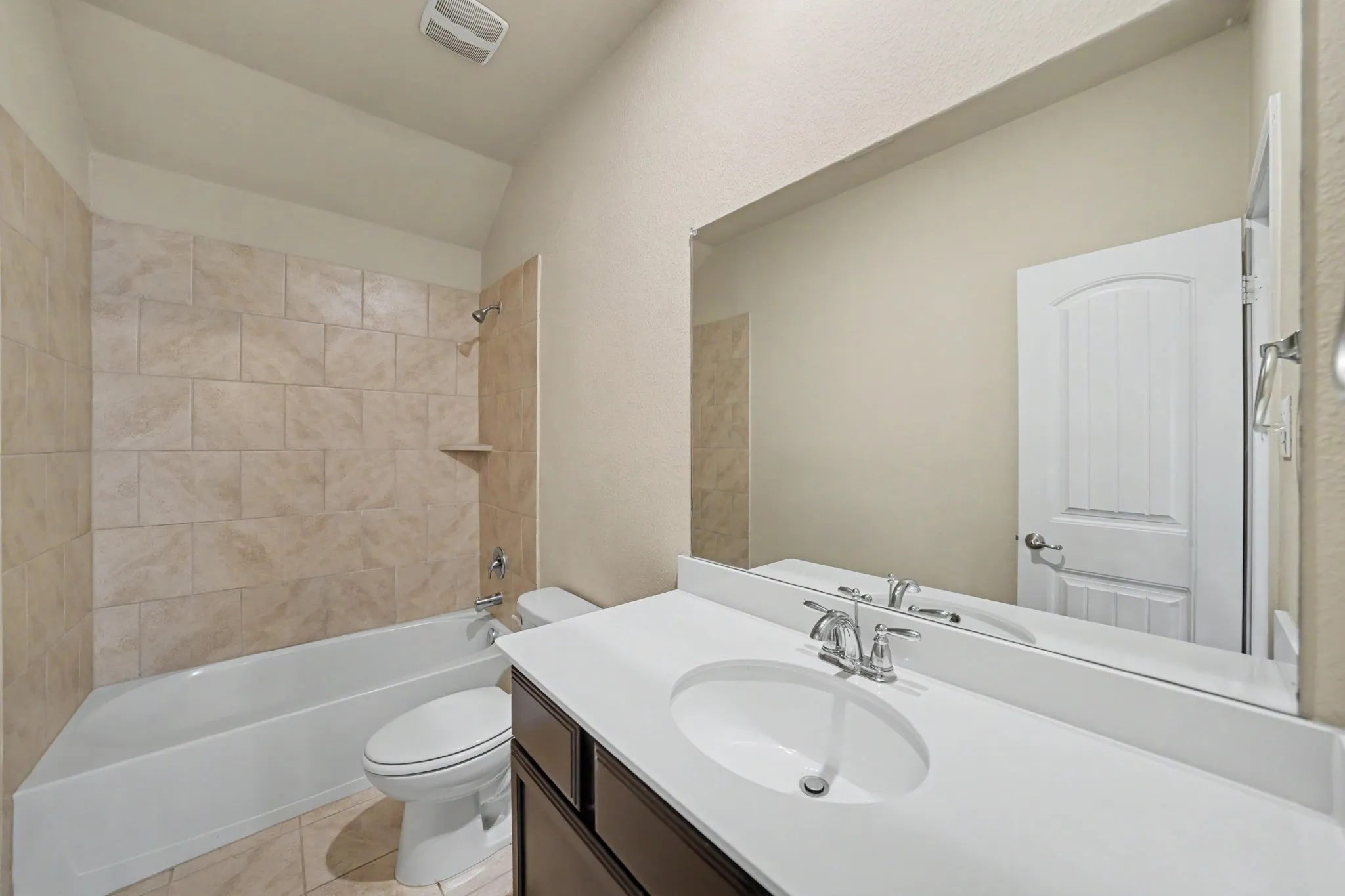 Bathroom featuring a built-in tub with neutral tile surround, a built-in vanity with an integrated sink, a large wall-mounted mirror, and tile flooring