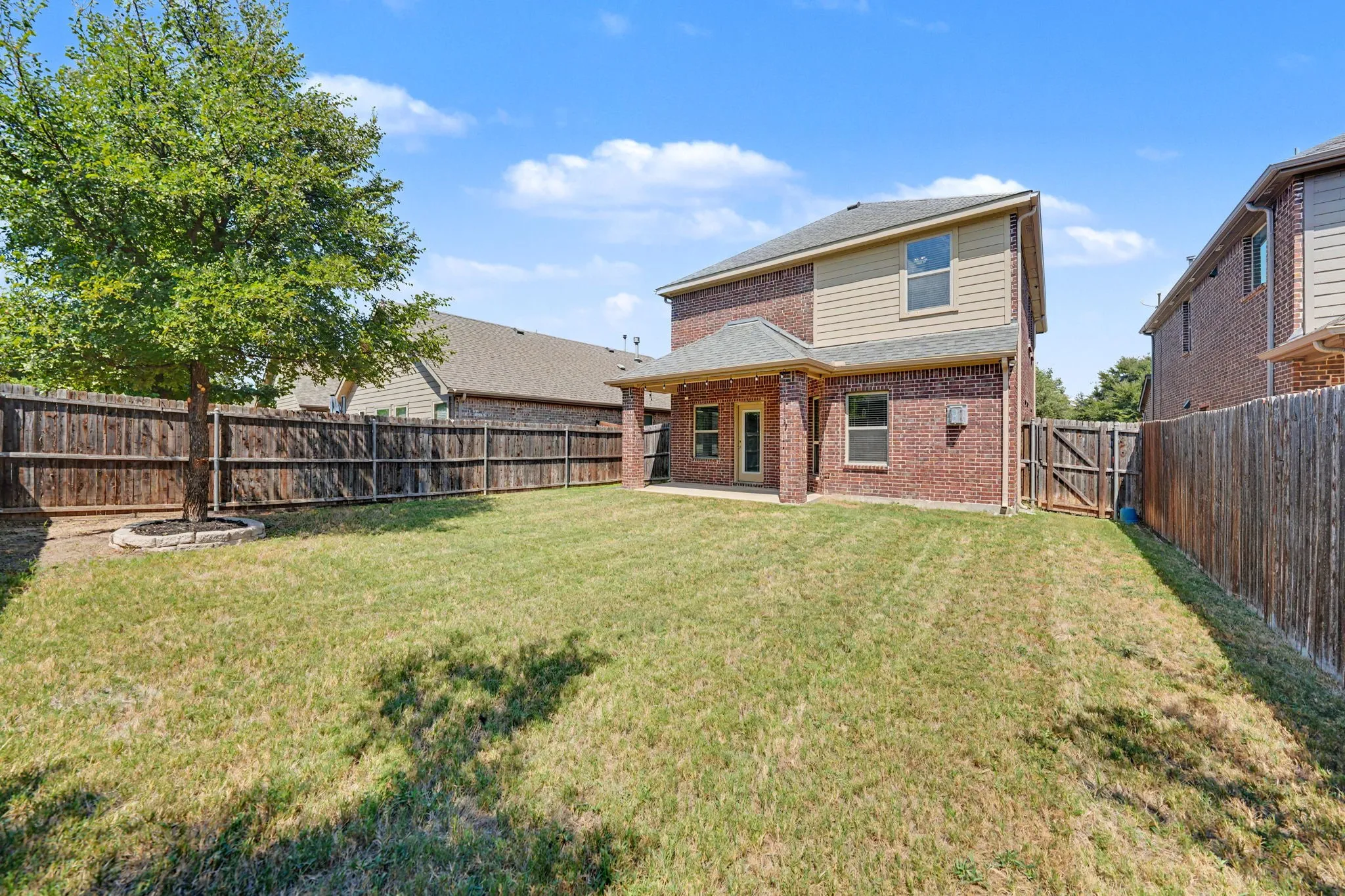 Expansive backyard featuring a manicured lawn, full privacy fencing, and a mature tree