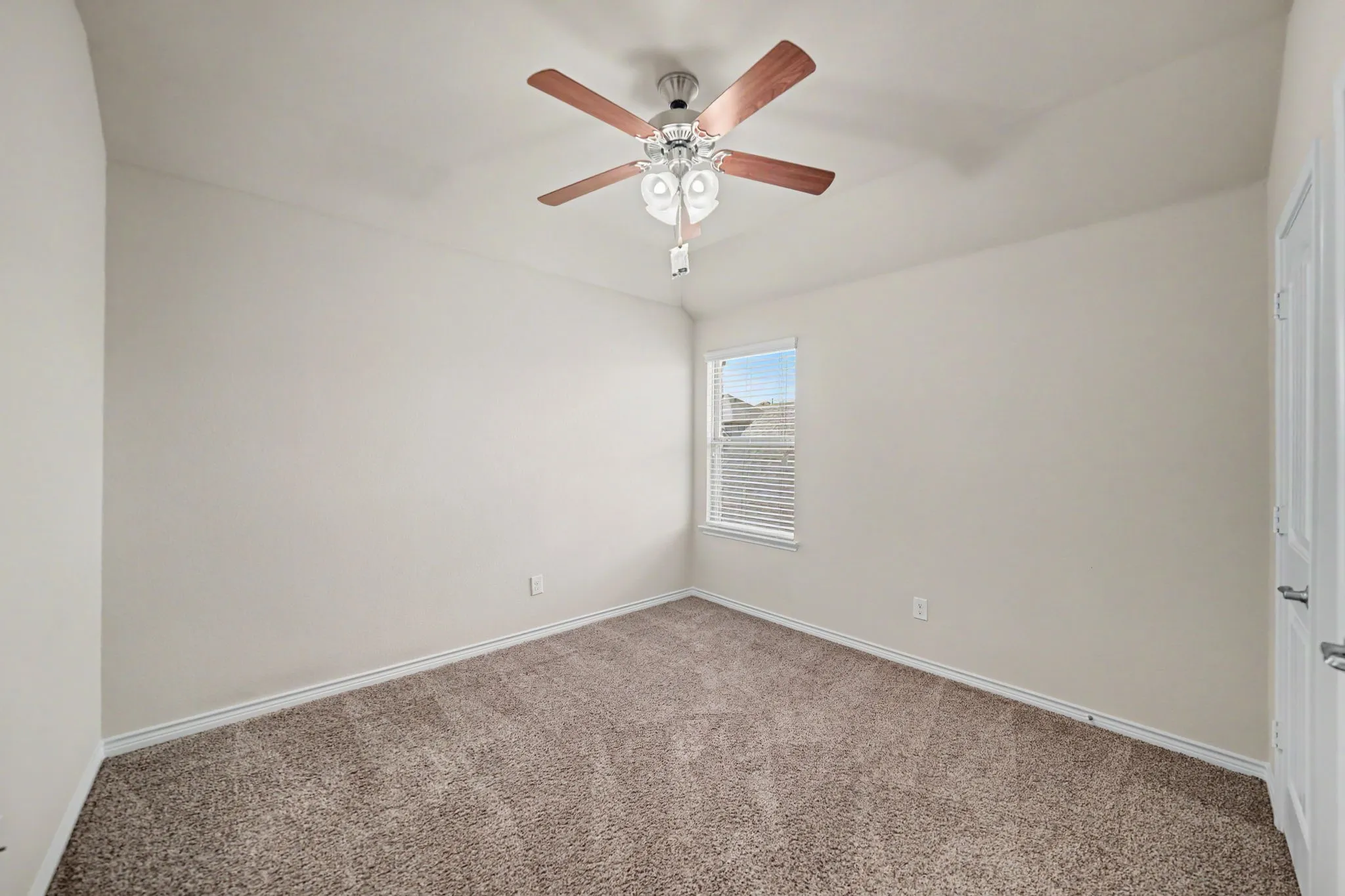 Plush carpet flooring, neutral painted walls, recessed window with blinds, ceiling fan with integrated lighting, and a white paneled door
