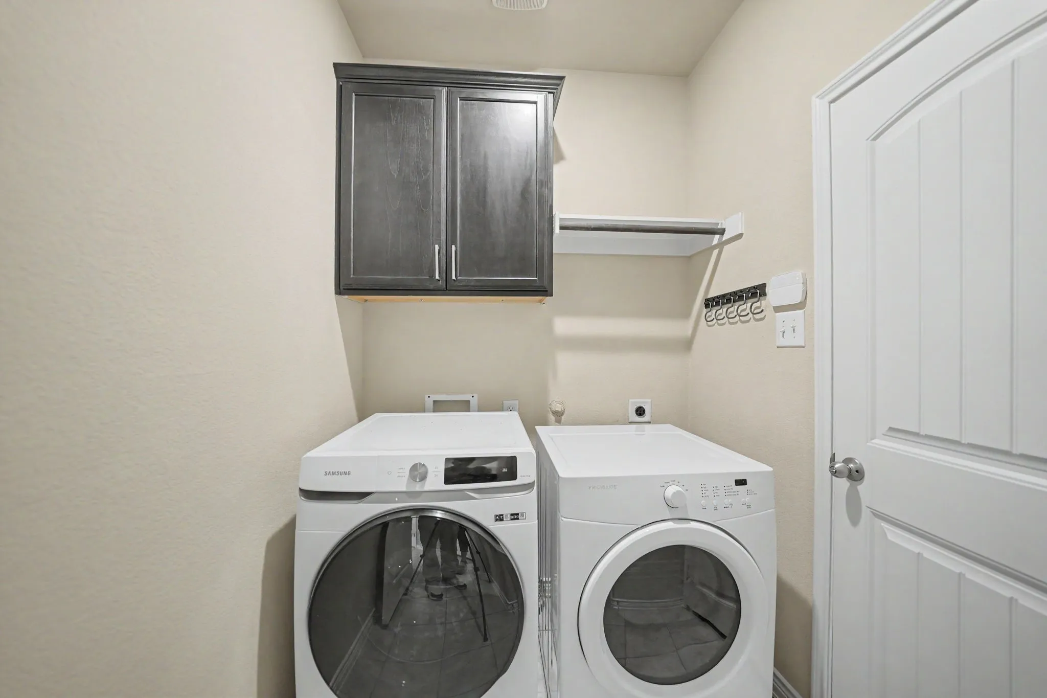 Laundry area featuring a dark wood-finish cabinet, white shelving, and a white panel door