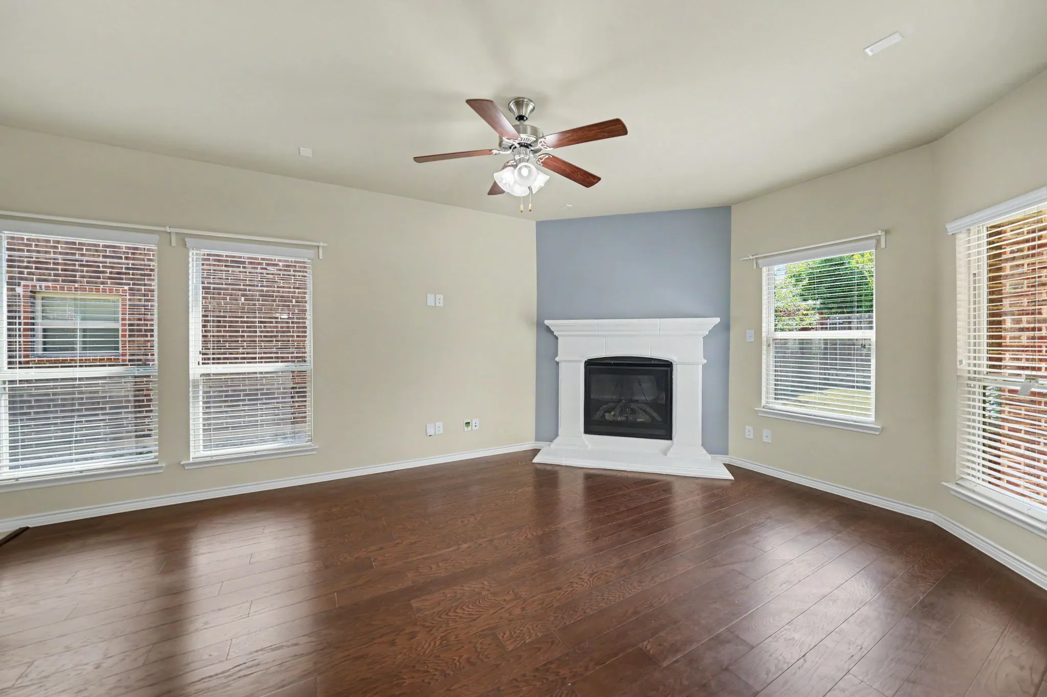 Expansive room featuring dark wood-finish flooring, a corner fireplace with a white mantel, and multiple windows