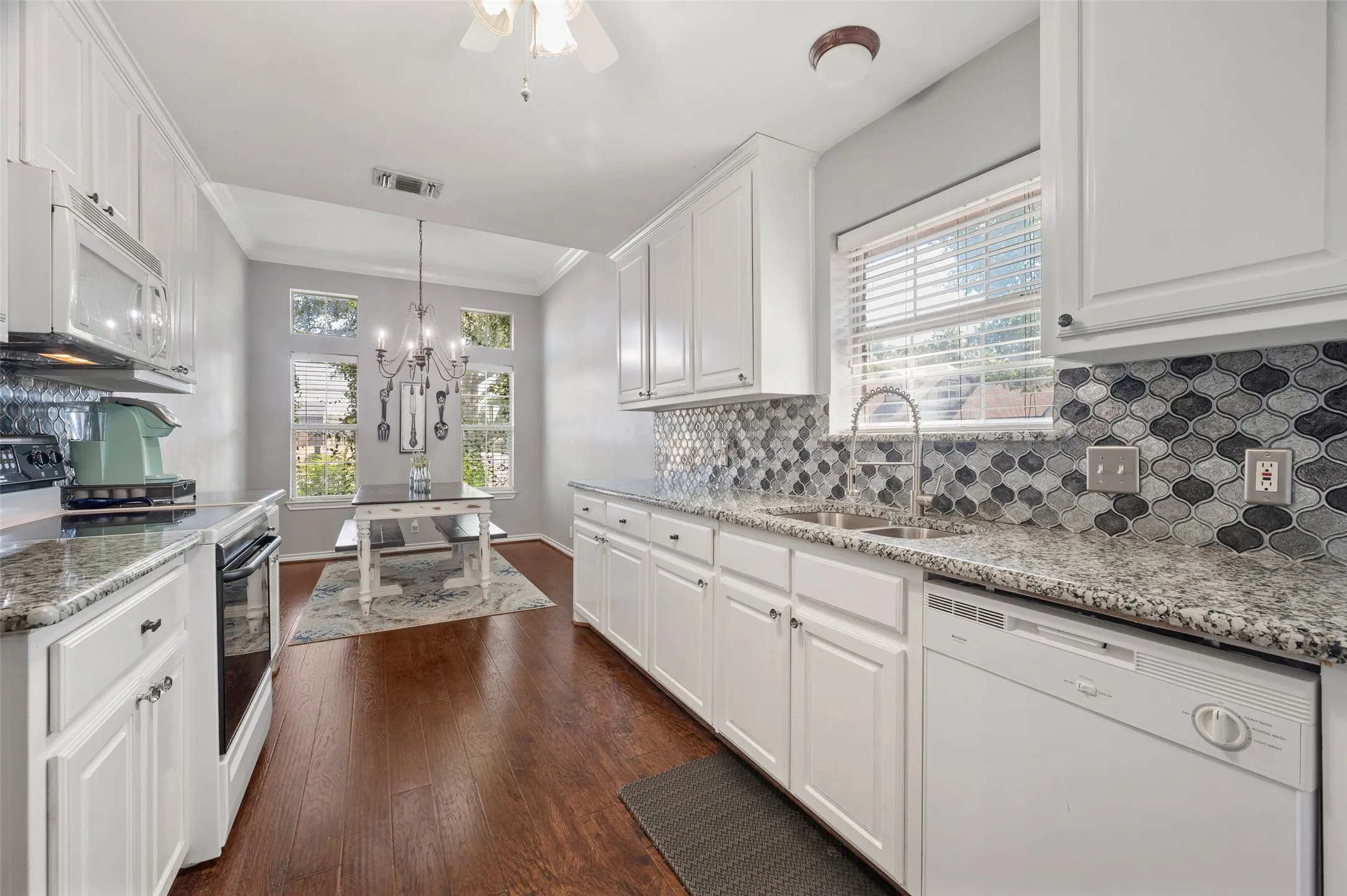 Beautiful kitchen has white painted cabinets with fresh hardware, custom backsplash with granite countertops and windows looking out onto a gardener's paradise.