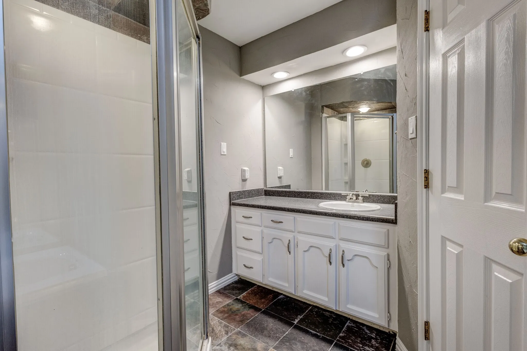 Shower enclosure with clear glass door, single vanity with integrated sink, dark countertop, recessed lighting, and tiled flooring