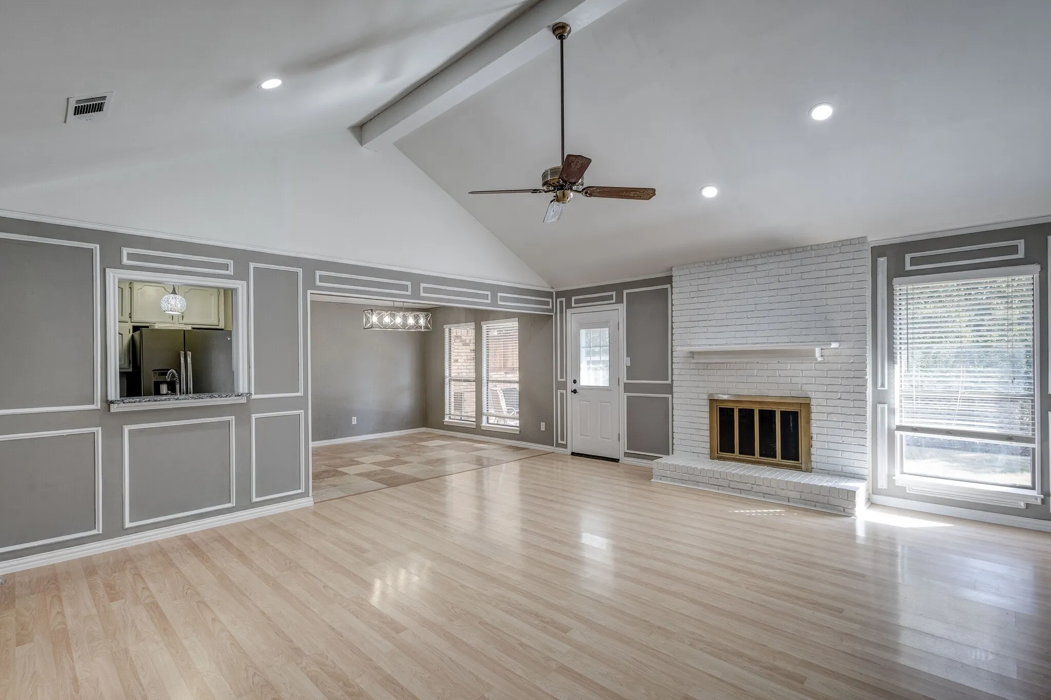 Vaulted ceiling with exposed beam, wood-finish flooring, white brick fireplace, wainscoting details, and recessed lighting